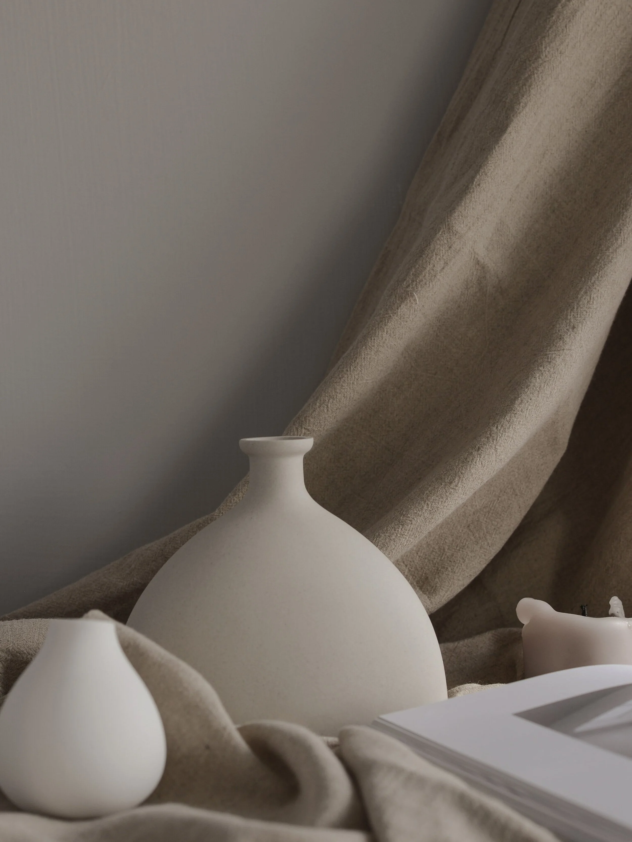 Close-up of white ceramic vases on a beige fabric surface with a beige curtain in the background.
