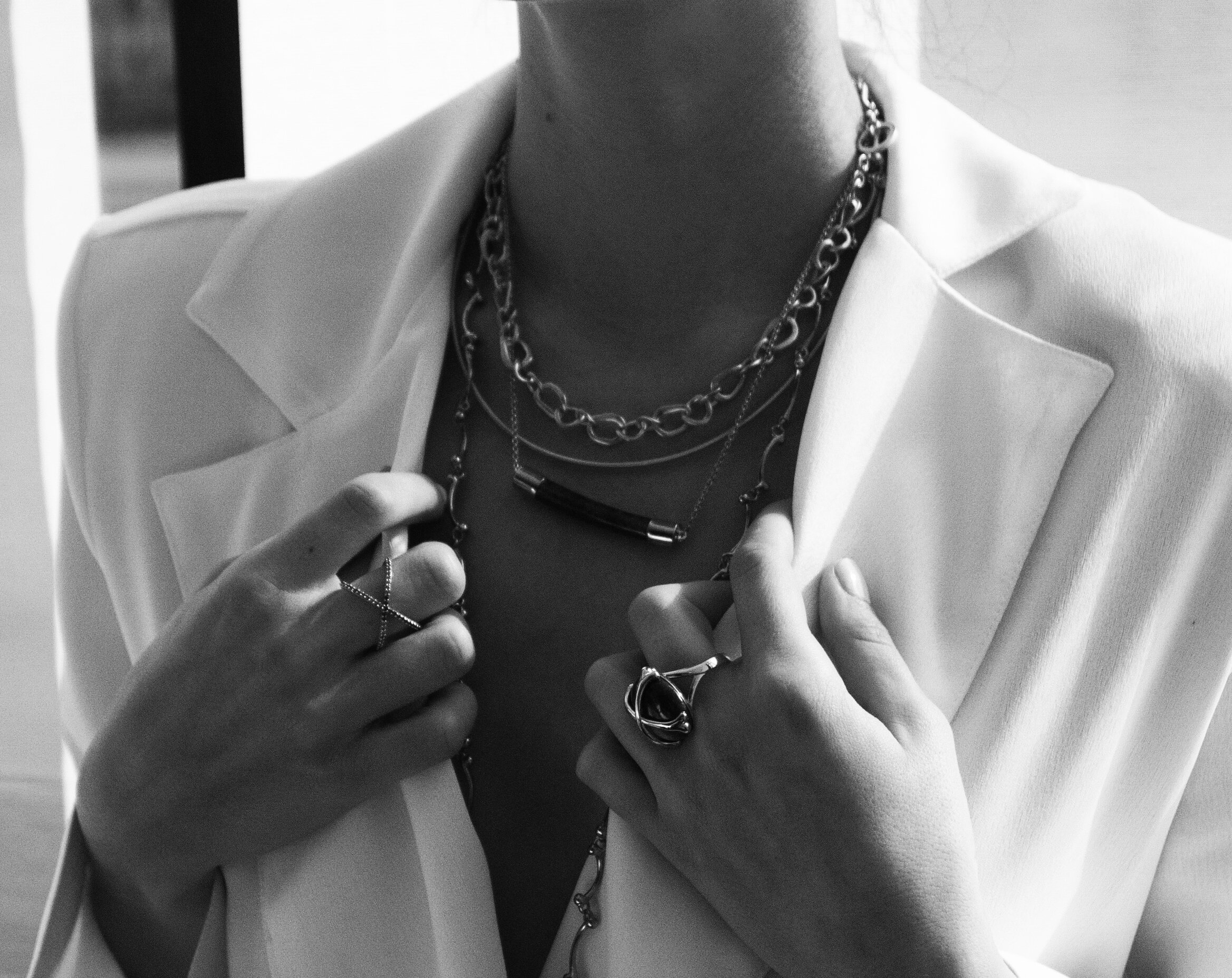 Close-up black and white photo of a woman wearing a white blazer and layered necklaces, holding a mobile phone.