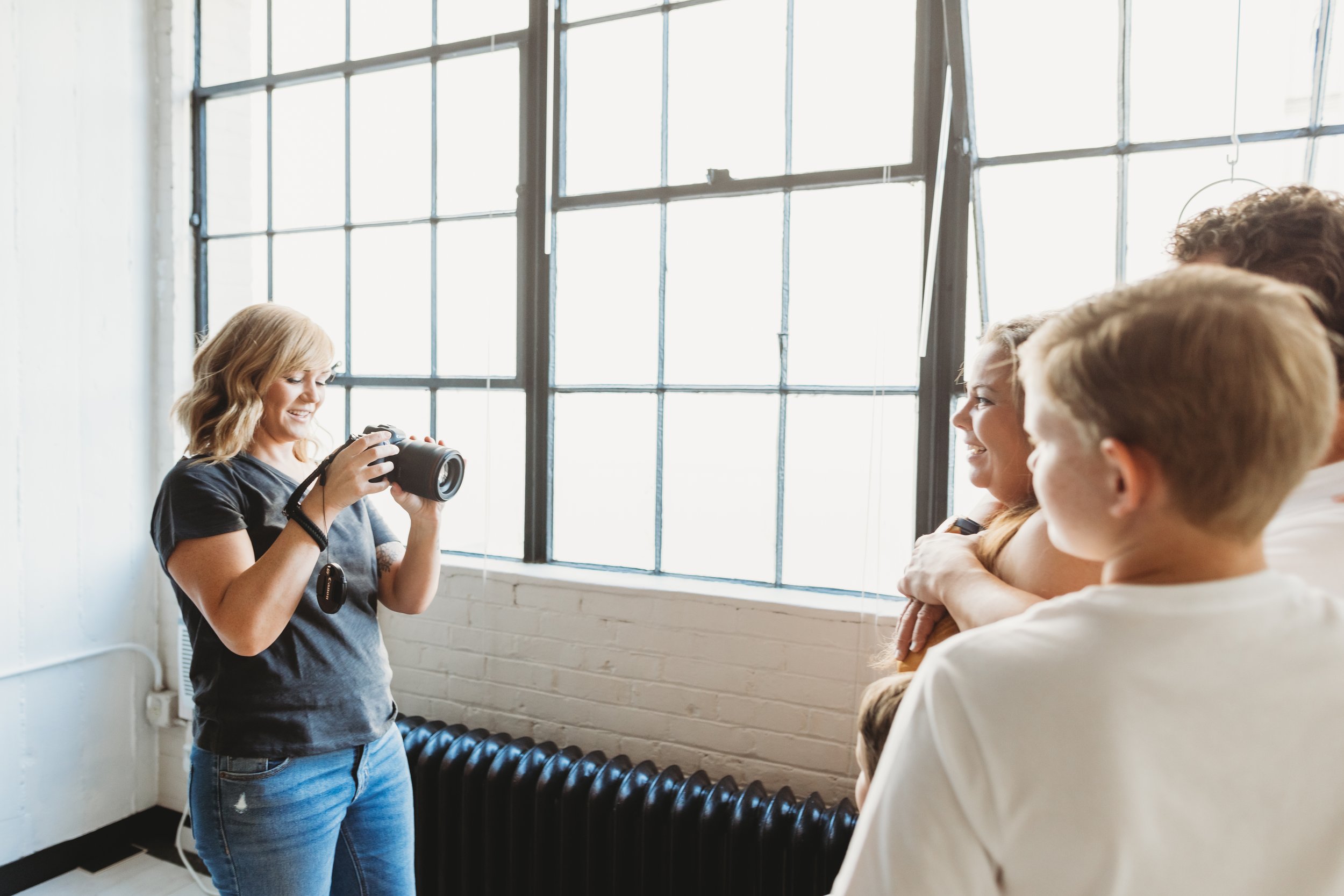 A woman taking a photo of a group of smiling friends near a large window in a bright studio.