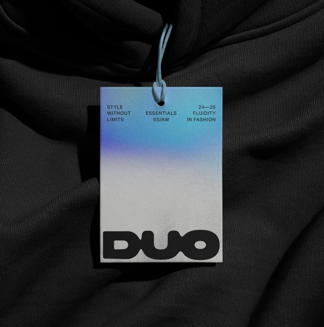 A premium DUO tag with a blue gradient, suspended over black textured fabric. The design emphasizes modern branding with minimalist typography, promoting fluidity in fashion and timeless essentials.