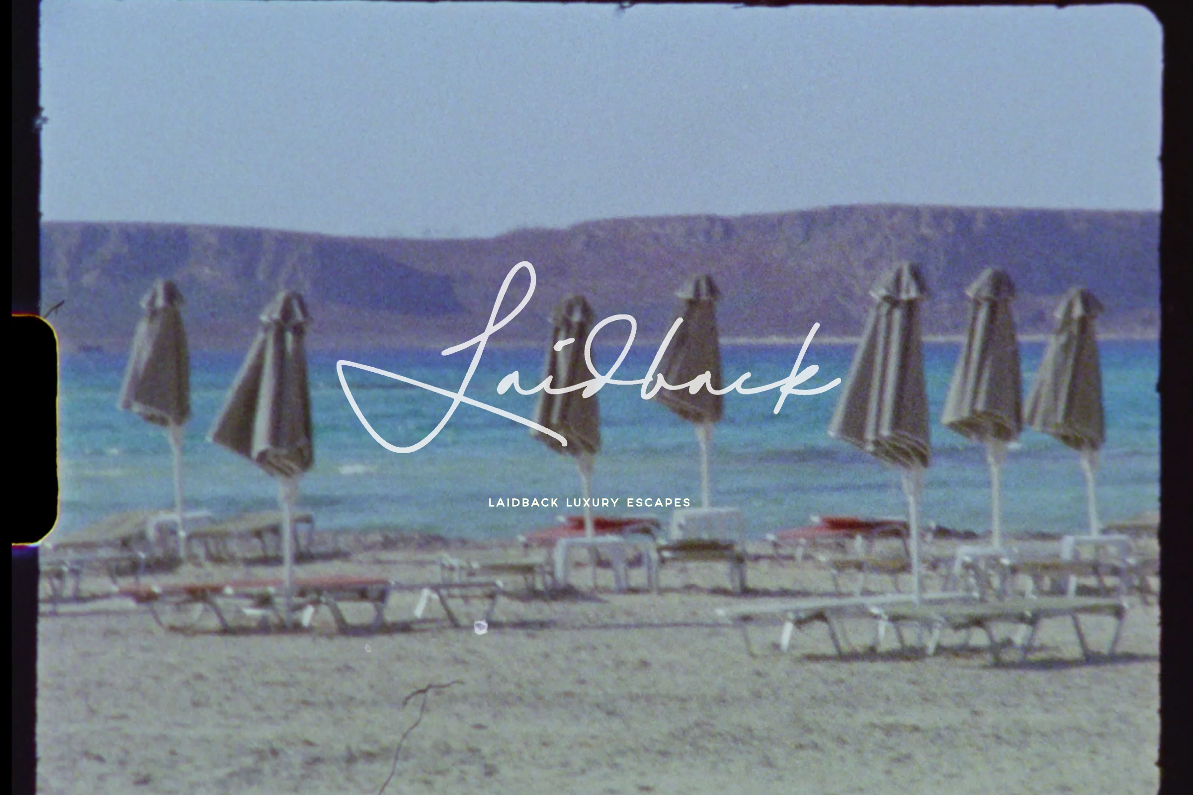 Beach scene with multiple closed beach umbrellas and lounge chairs on a sandy shore, with mountains and water in the background, and text overlays reading "Lighthouse" and "Laidback Luxury Escapes."