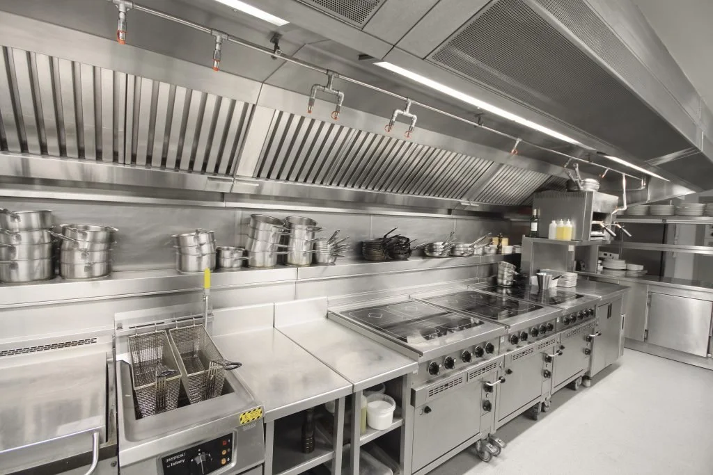 Commercial stainless steel kitchen with cooking stove, pots, utensils, and storage shelves.