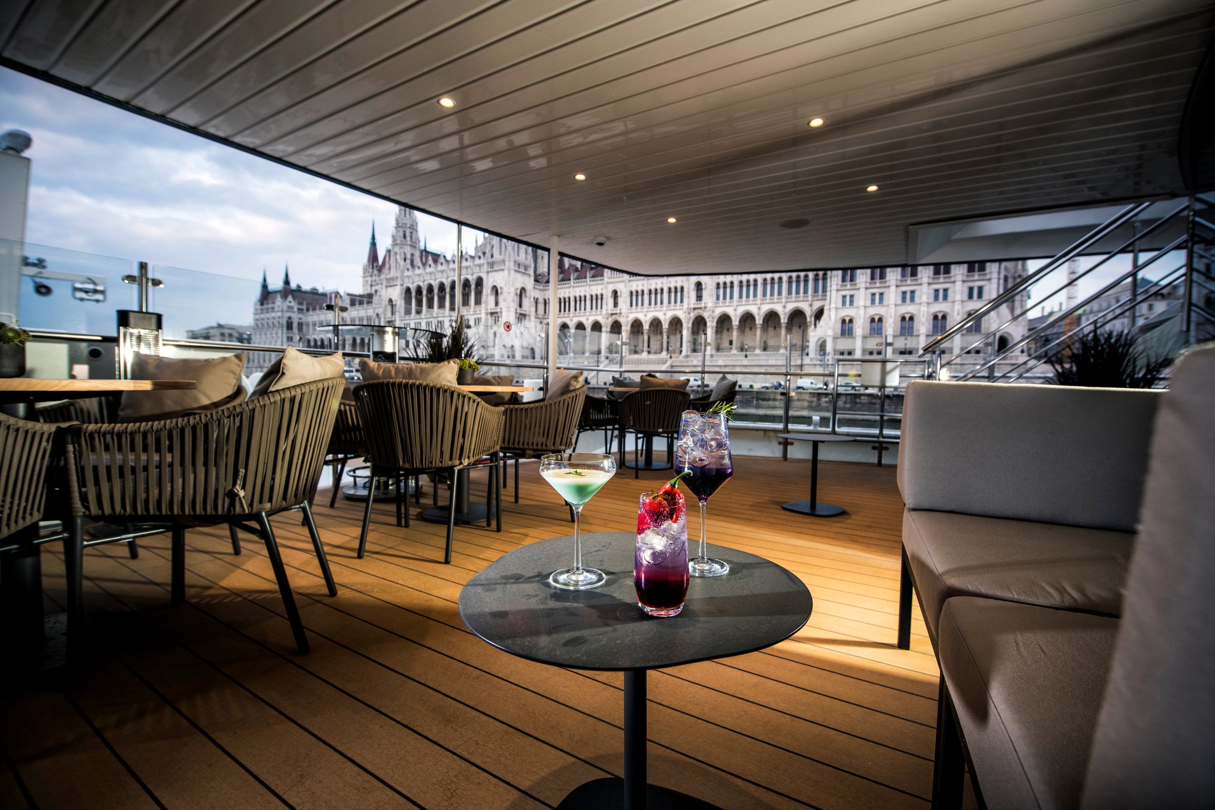 View from a restaurant or bar with several cocktails on the table, wicker chairs, and a view of historic buildings outside.