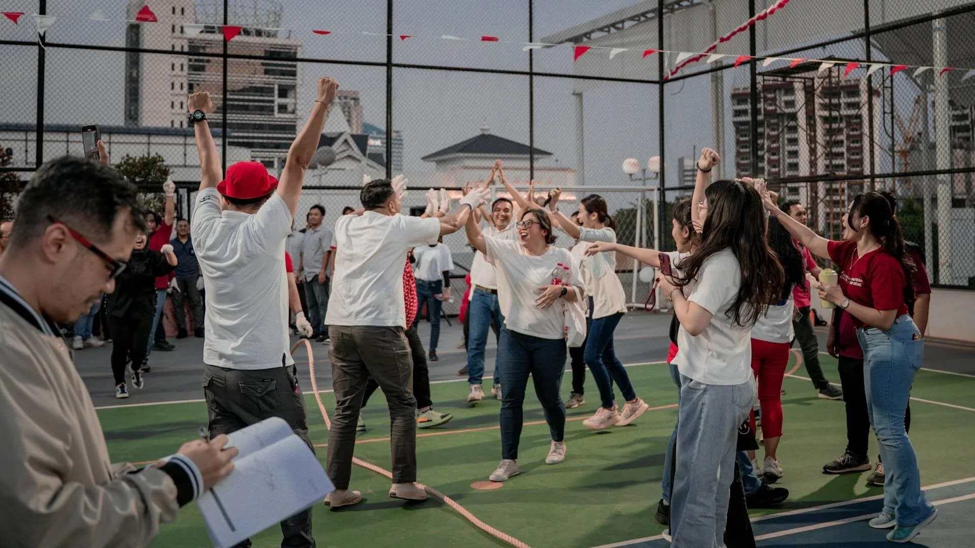 Group of people on a rooftop court dancing and celebrating, some high-fiving, with city buildings in the background.