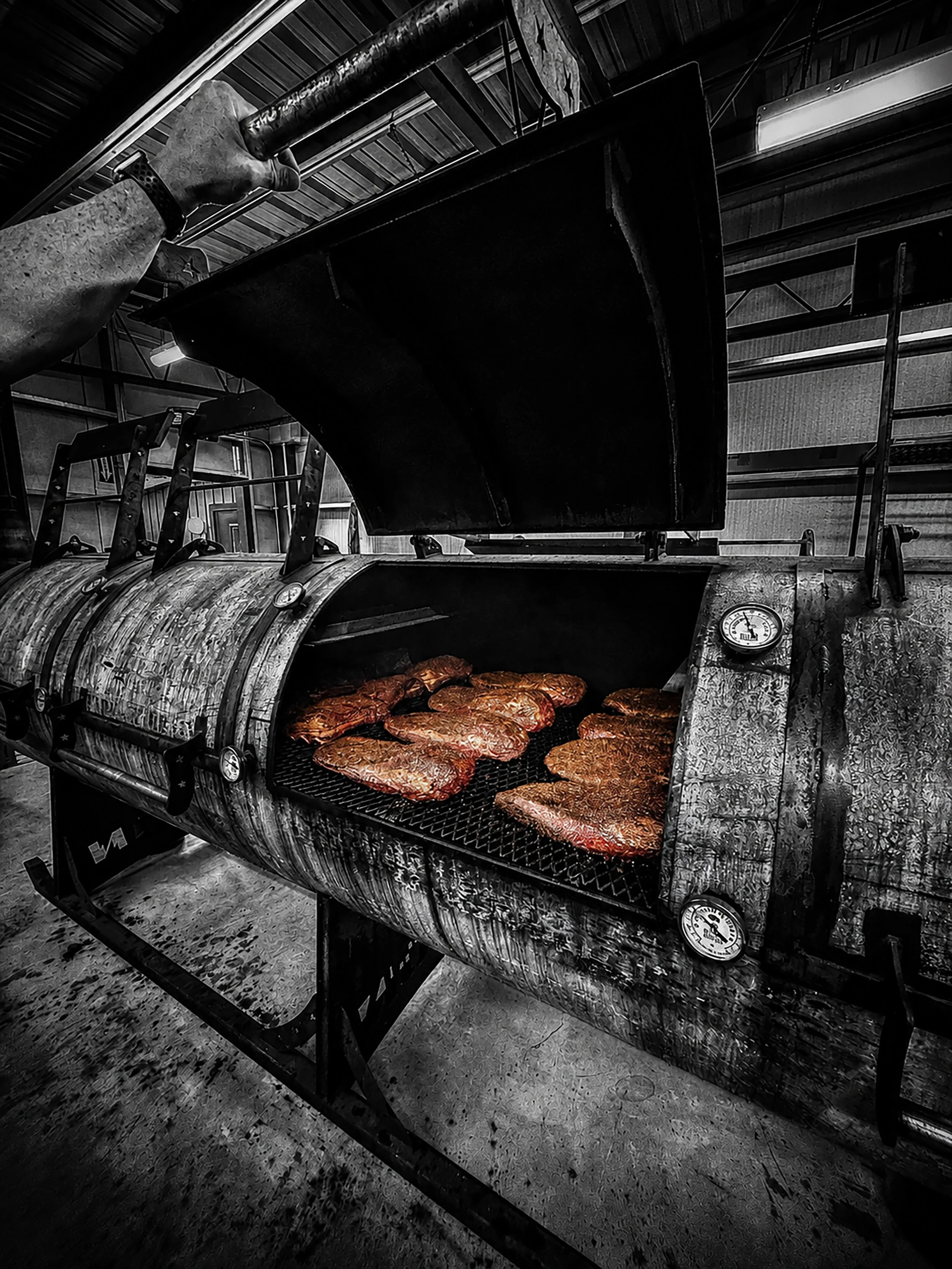 Meat being cooked in an outdoor grill, with a barbecue thermometer attached to the side.