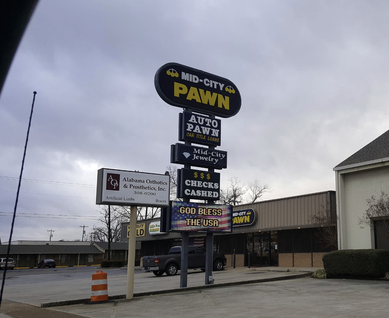 Signage outside Mid-City Pawn shop displaying various advertisements and services, including auto pawn, jewelry, check cashing, and a message reading 'God Bless the USA.'