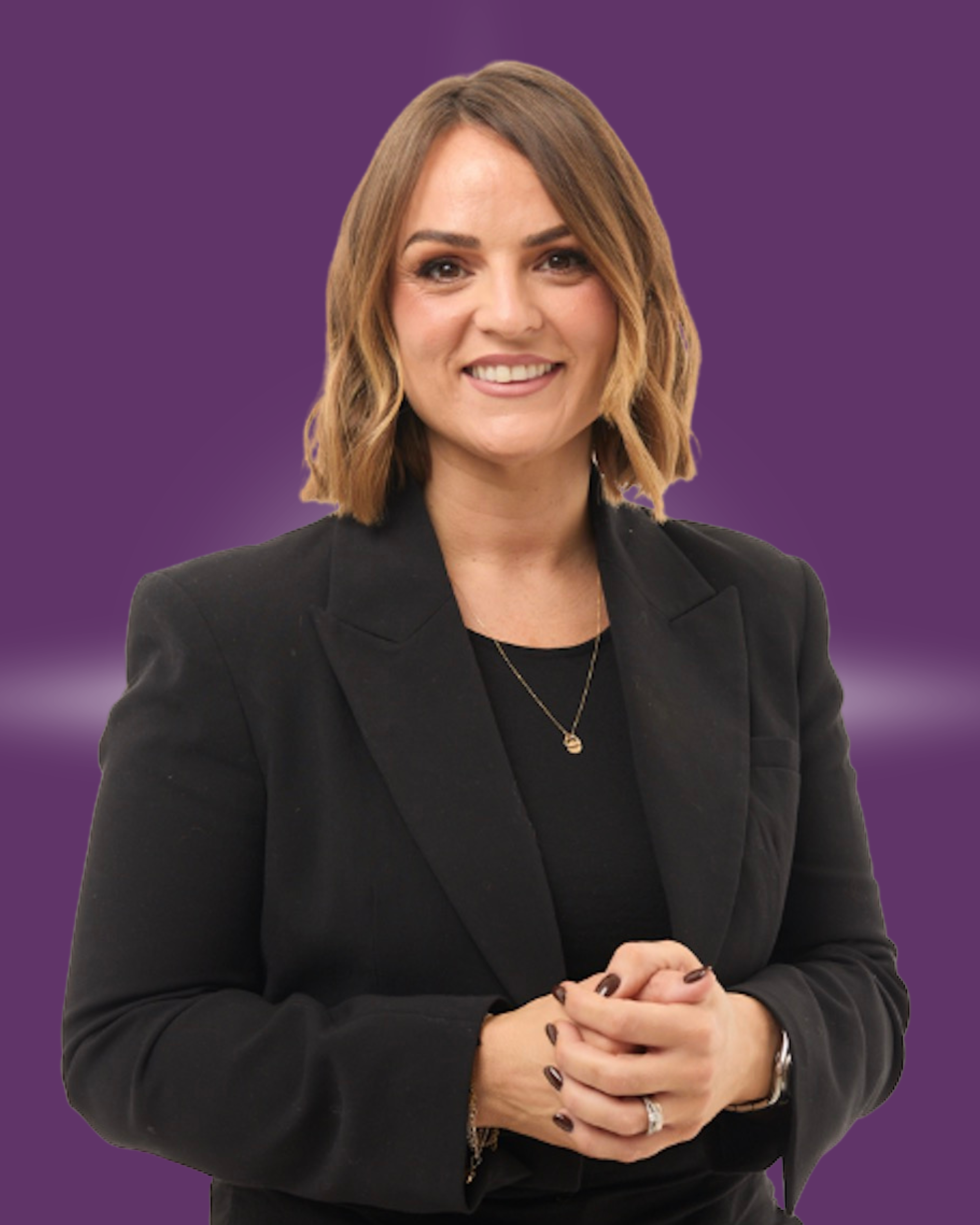 A woman with shoulder-length brown hair smiling, wearing a black blazer, black top, gold necklace, and ring, with a purple background.