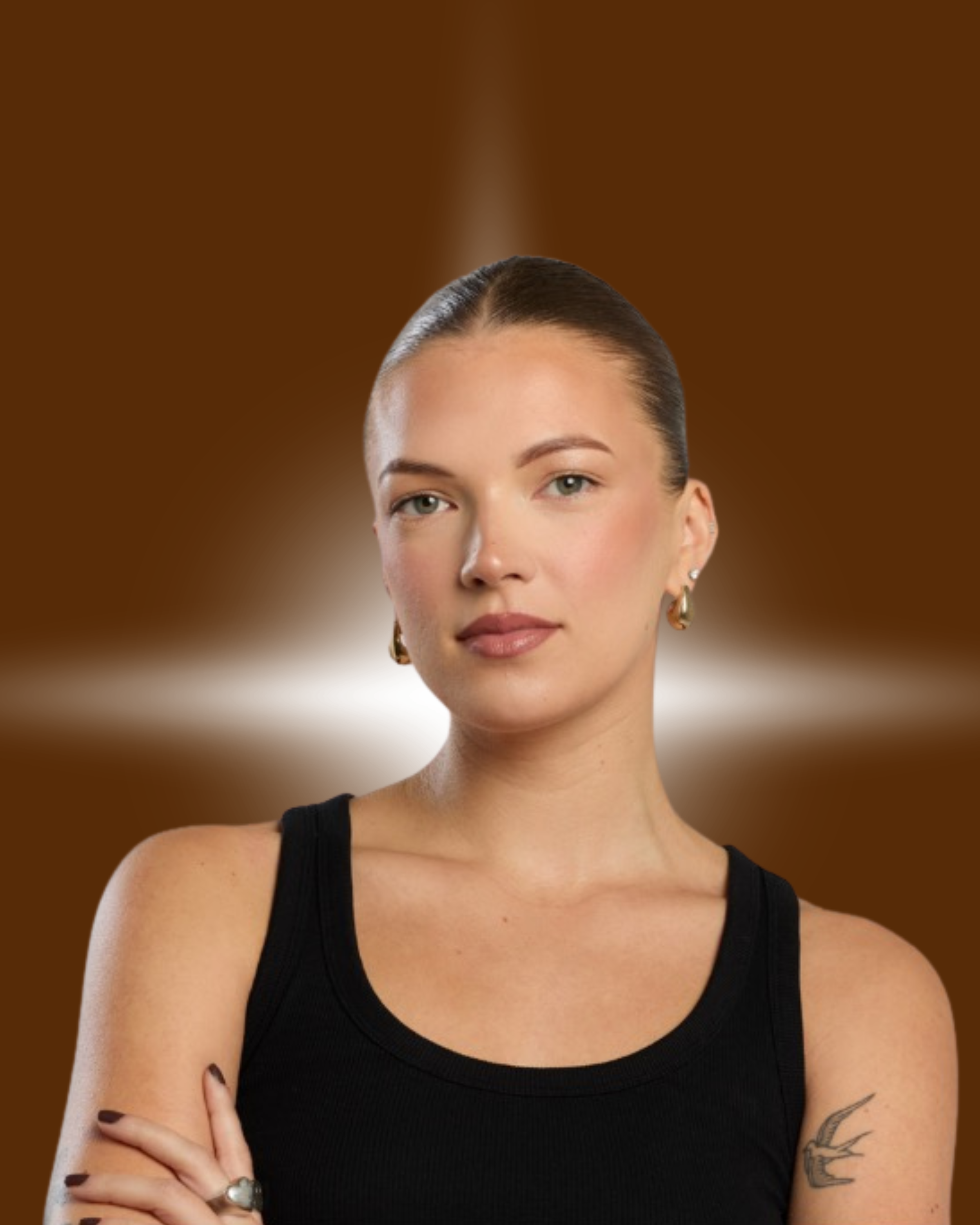 Portrait of a woman with a confident expression, wearing a black tank top and gold earrings, with a tattoo of a swallow on her upper arm, set against a brown background with a bright light behind her head.