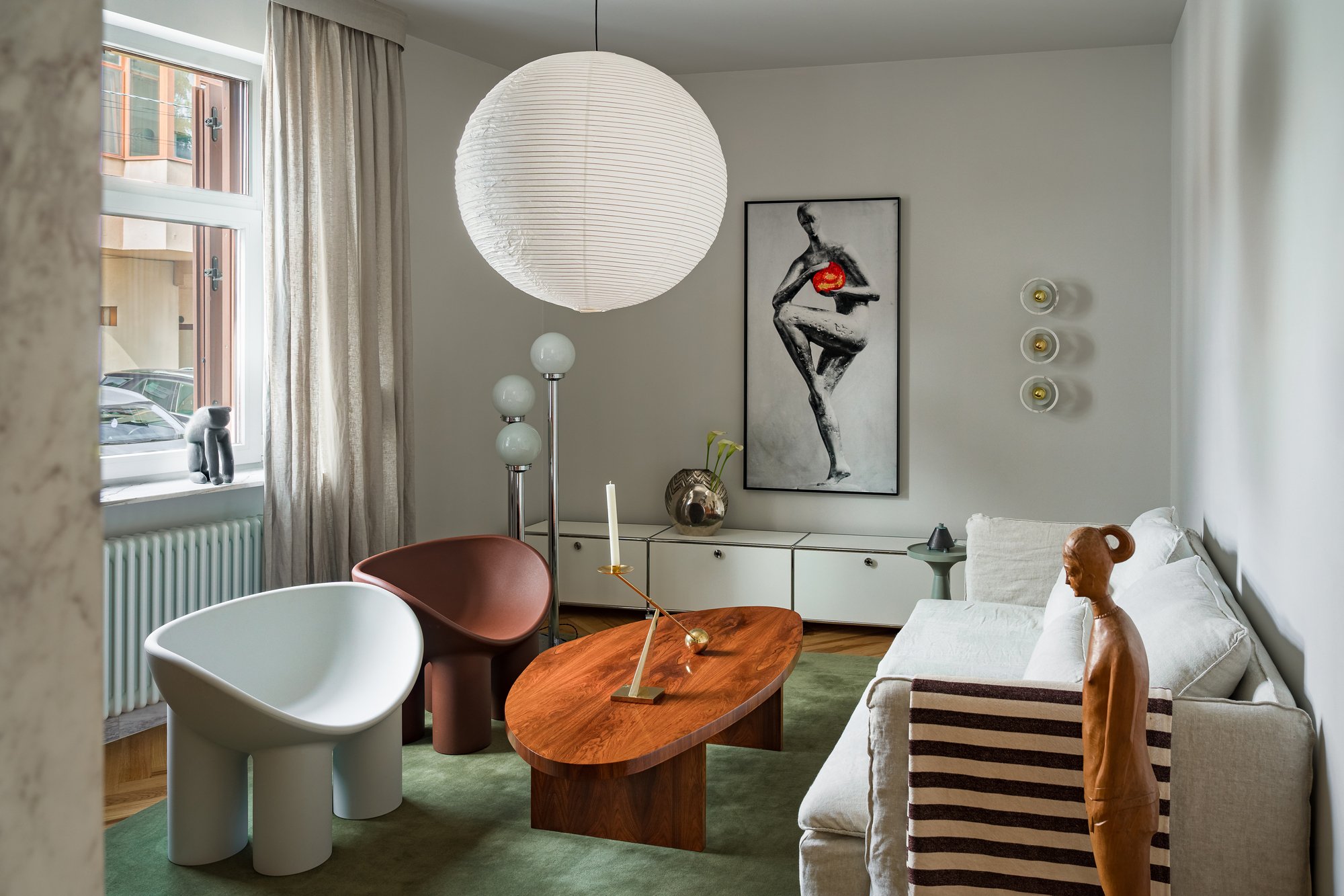 Living room with a white sofa, wooden coffee table, modern chairs, artwork on the wall, and decorative objects.