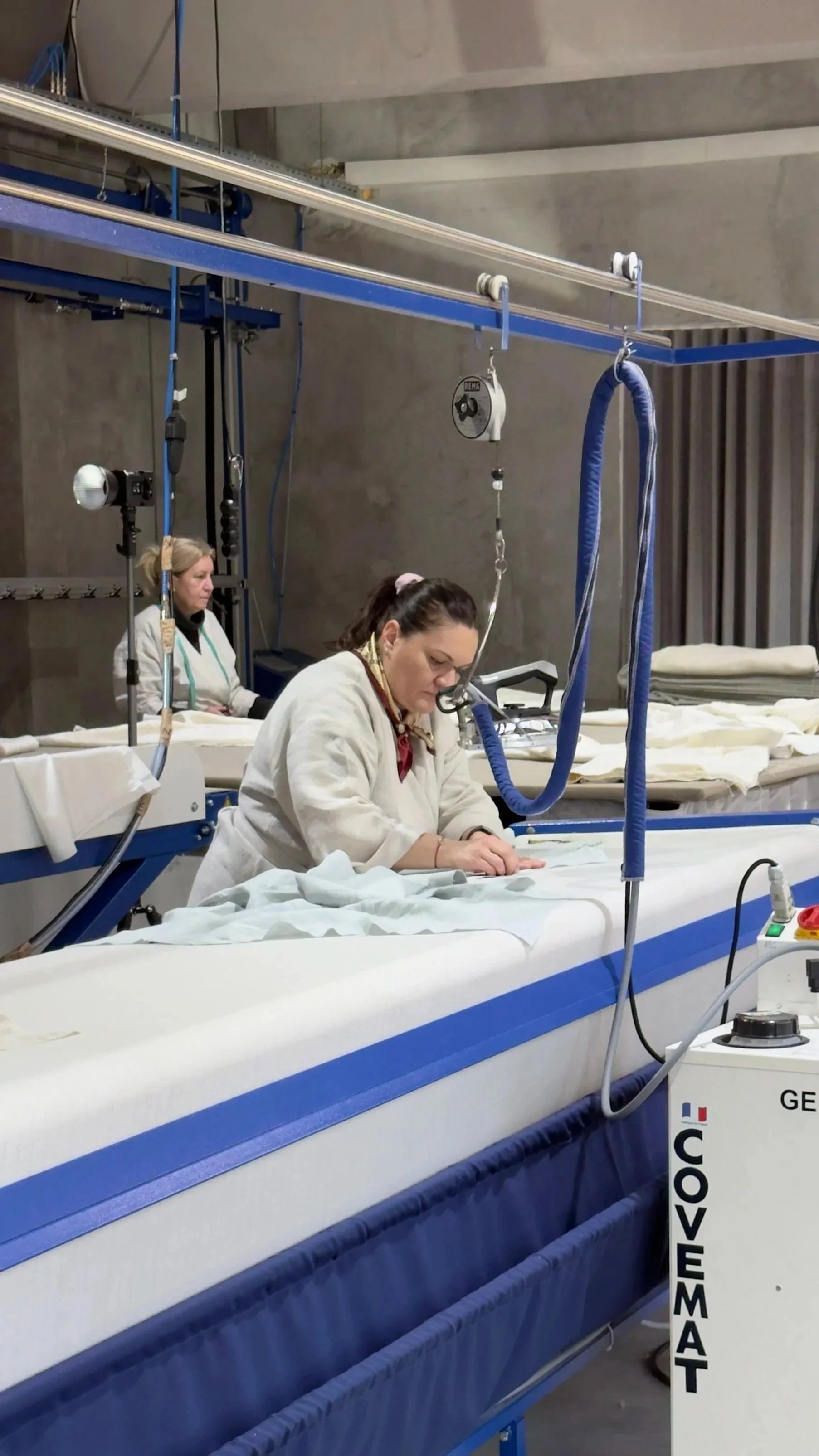 Two women working in a cleanroom, assembling or inspecting medical or technological equipment on a long worktable with specialized machinery.