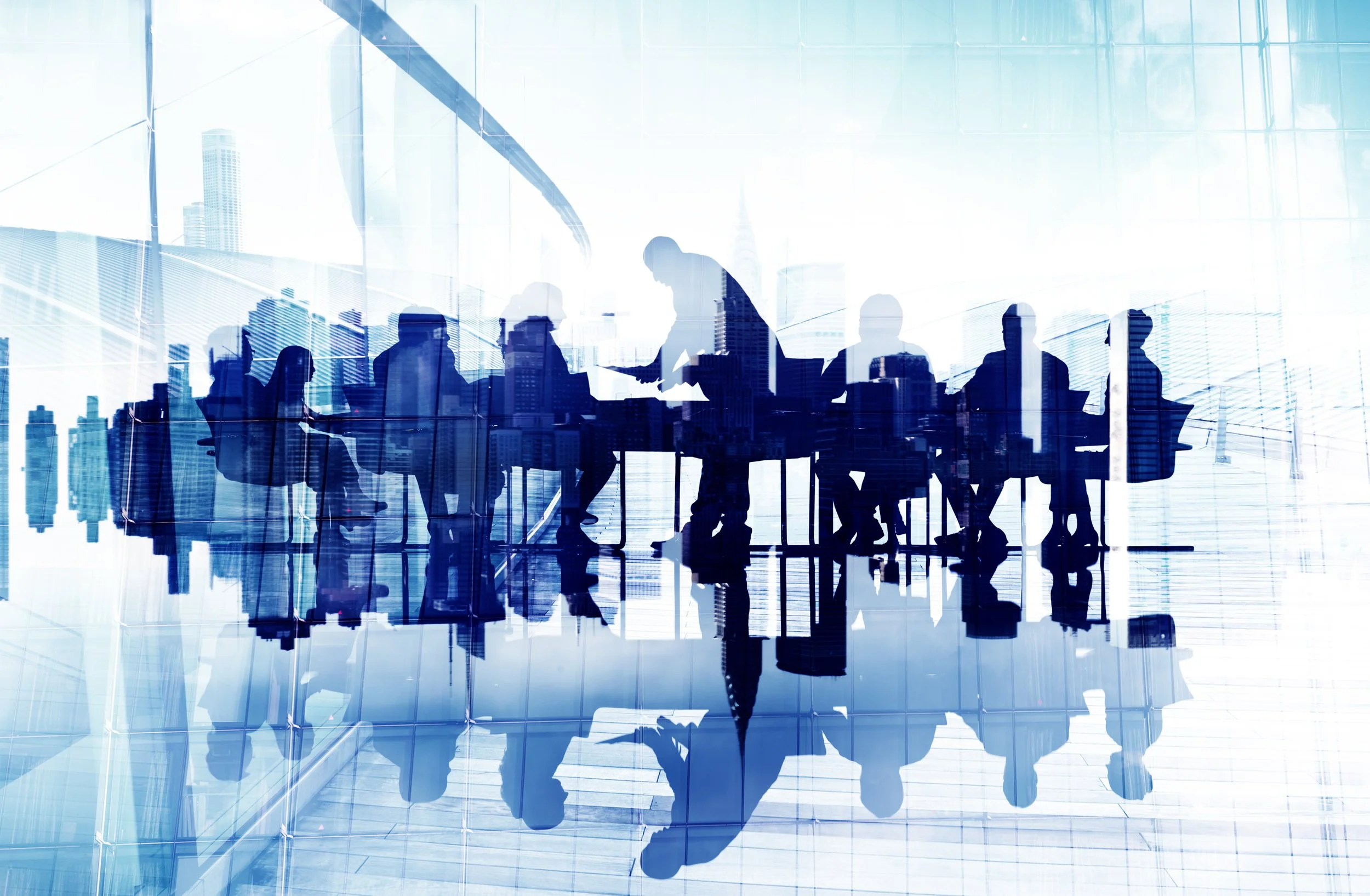 Silhouettes of business people in a meeting room with a city skyline reflected in the glass wall