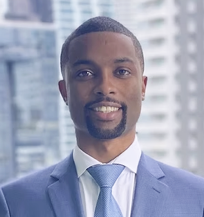 A man in a blue suit and tie smiling against a cityscape background.