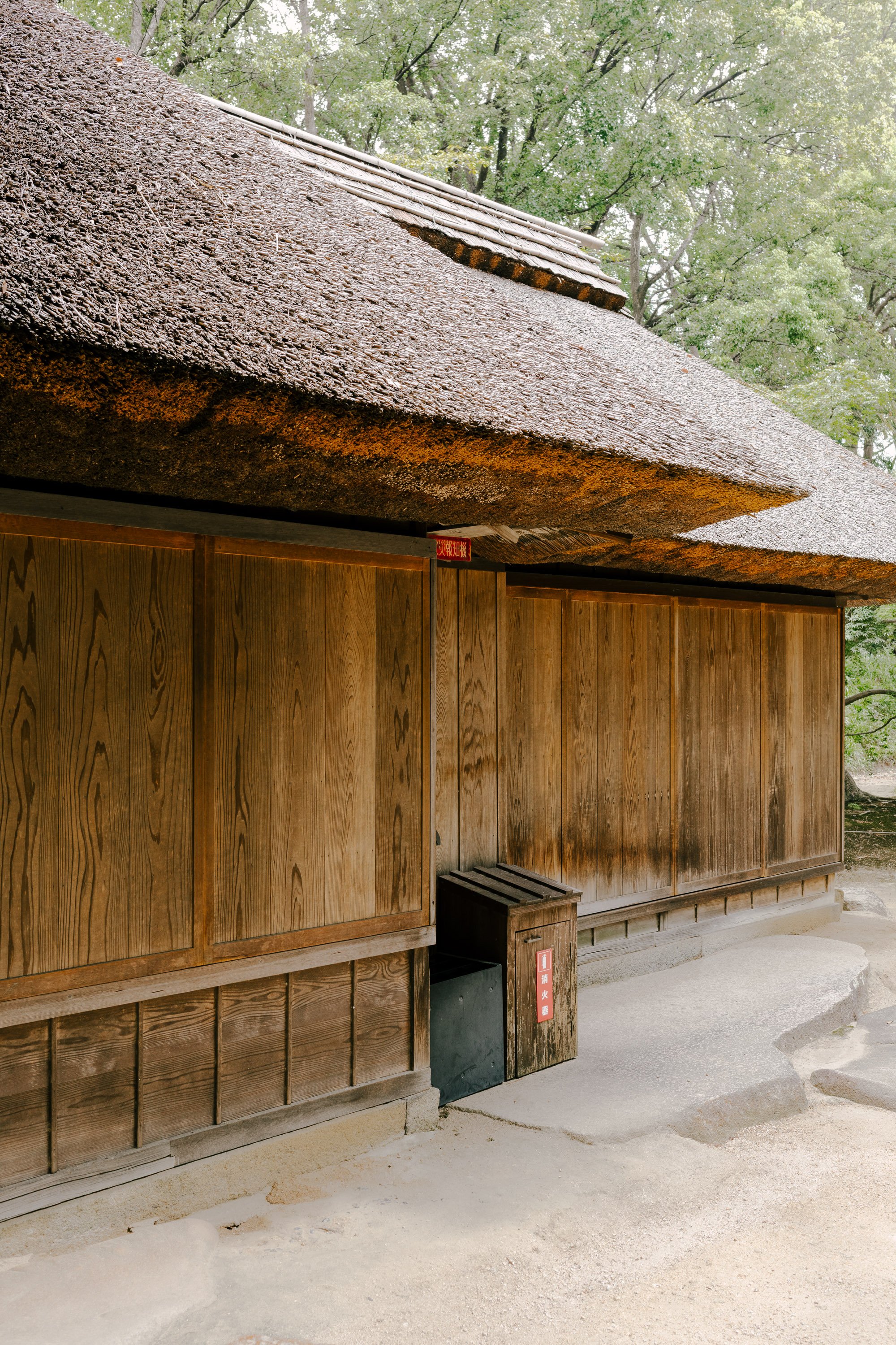 A traditional Japanese wooden building with a thatched roof, surrounded by trees.