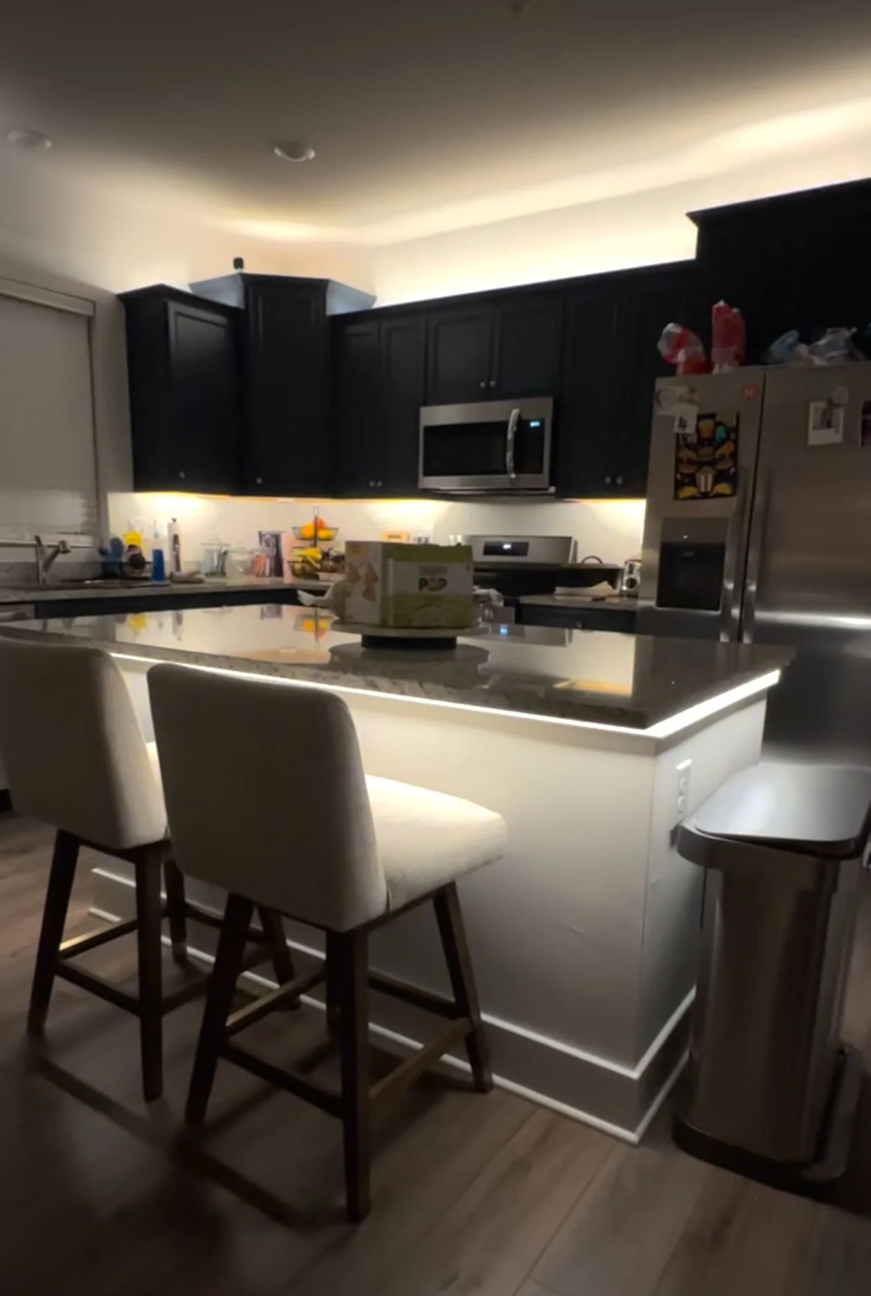 A kitchen with dark blue cabinets, lit with warm white LED lighting, and a kitchen island lit with warm white LEDs.