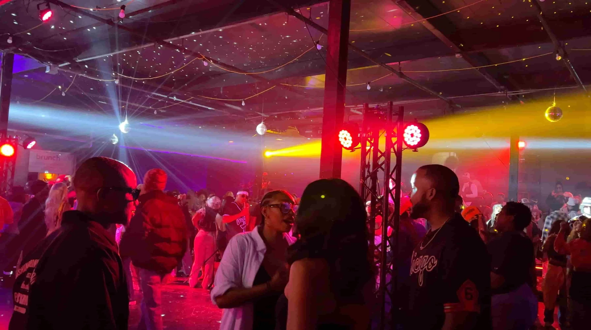 People dancing and socializing at a lively party with colorful stage lights and disco balls.
