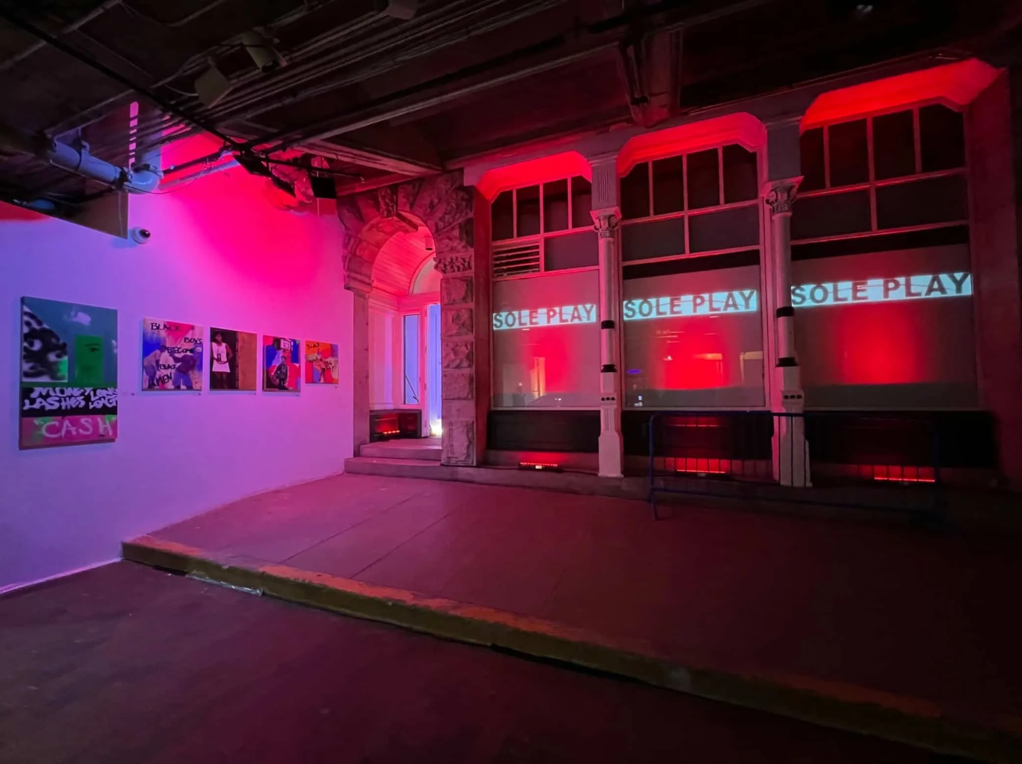 Temporary Art gallery installation with purple and red lighting, displaying colorful artwork on the wall and large windows with the words 'SOLE PLAY' projected onto them. Created during Atlanta Fashion Week.