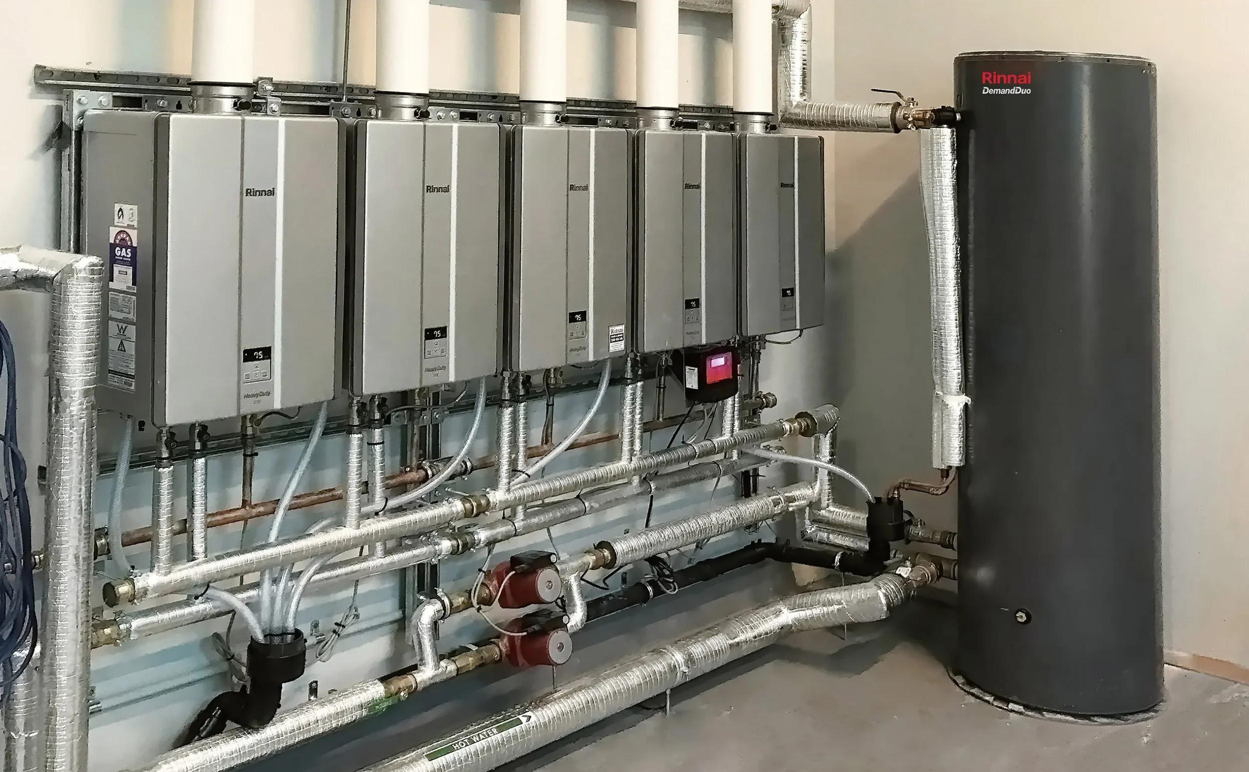 A commercial water heating and circulation system with multiple control units, pipes, and a large vertical storage tank.