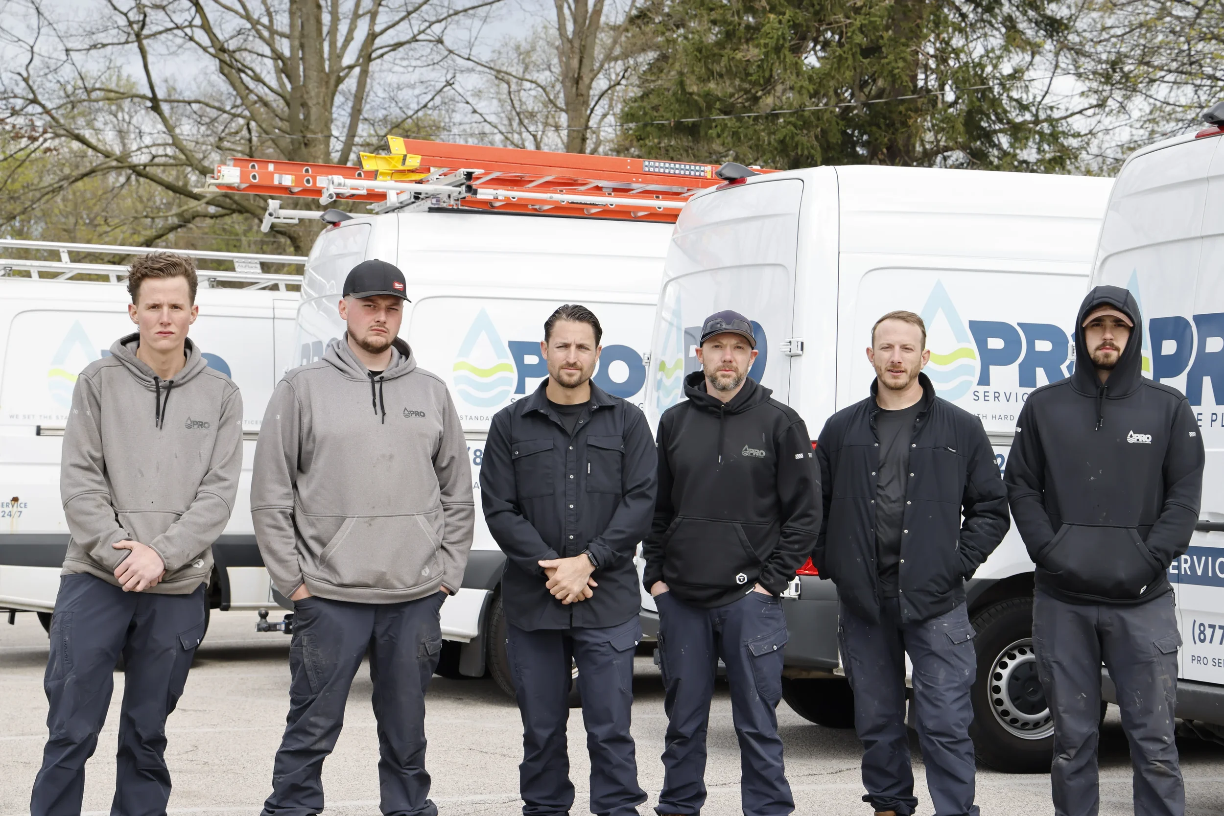 Pro Service Plumbers standing in front of service vans with ladder racks, wearing work clothes.