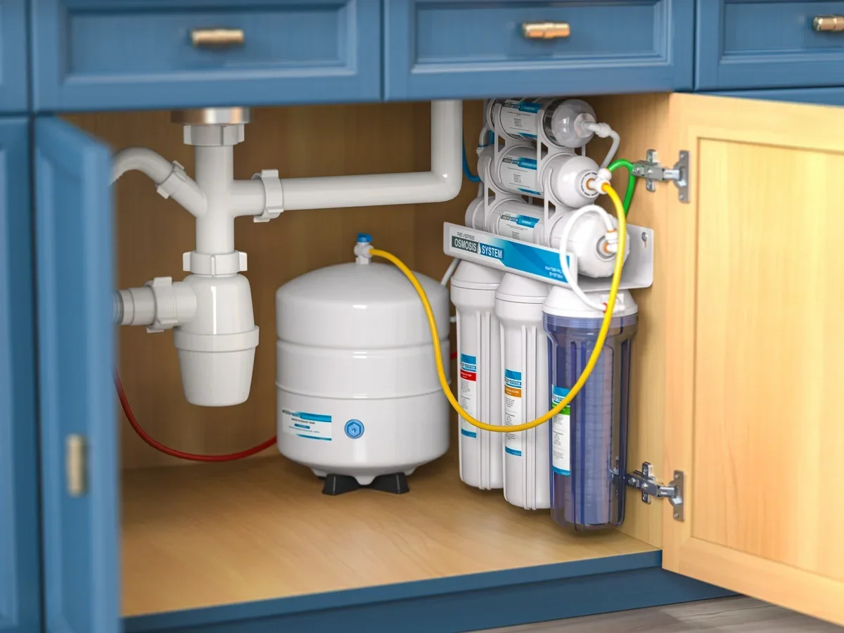 Under kitchen sink with water filtration system and pipes.