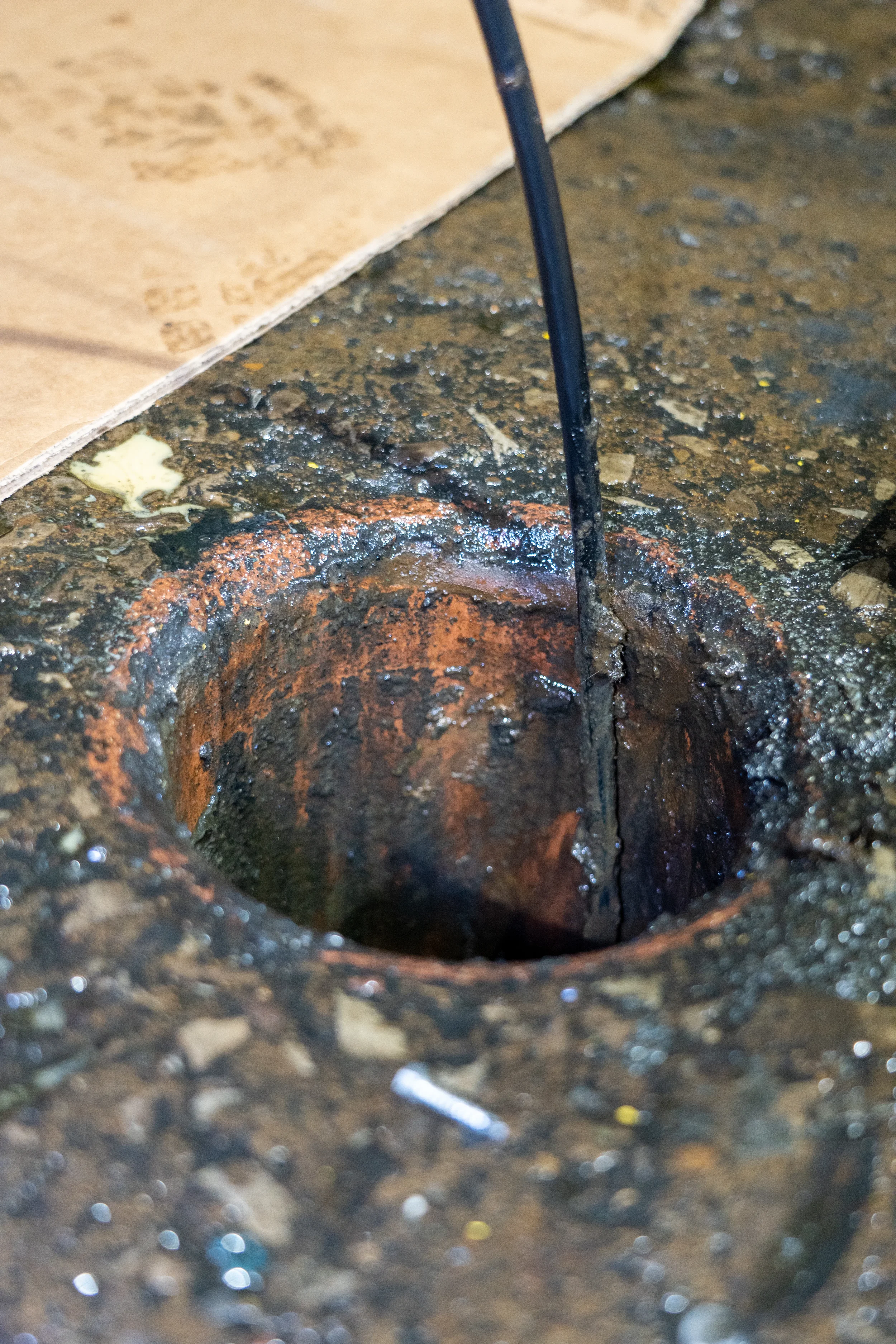 Close-up of a rusty, clogged drain with black pipe.