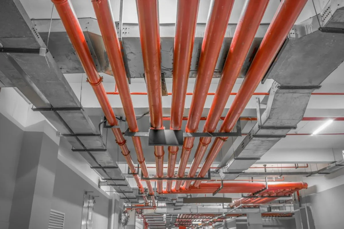 Ceiling with multiple orange pipes and gray metal ducts in an industrial or commercial building.