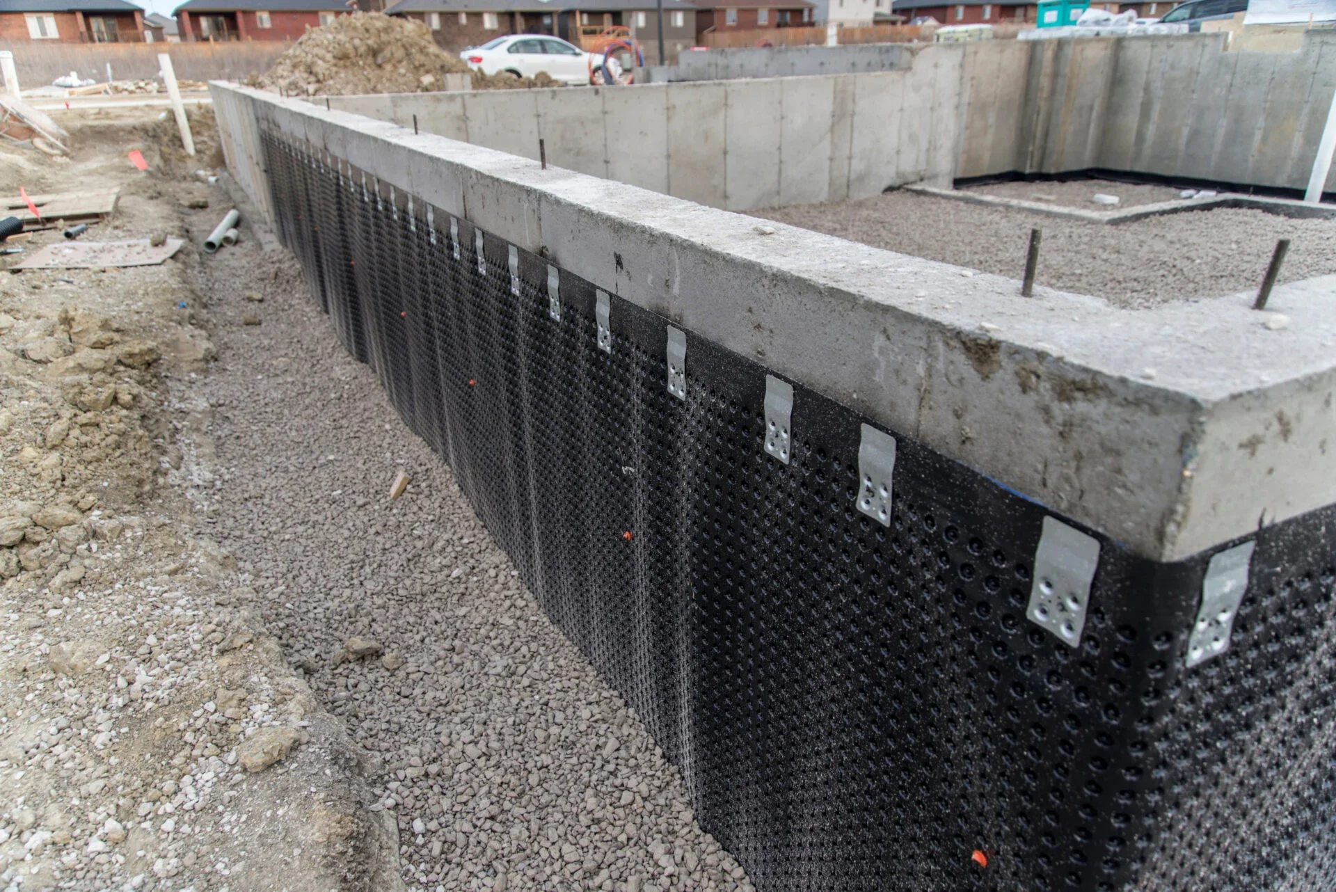 Construction site showing a concrete foundation with basement waterproofing membrane along the bottom edge.