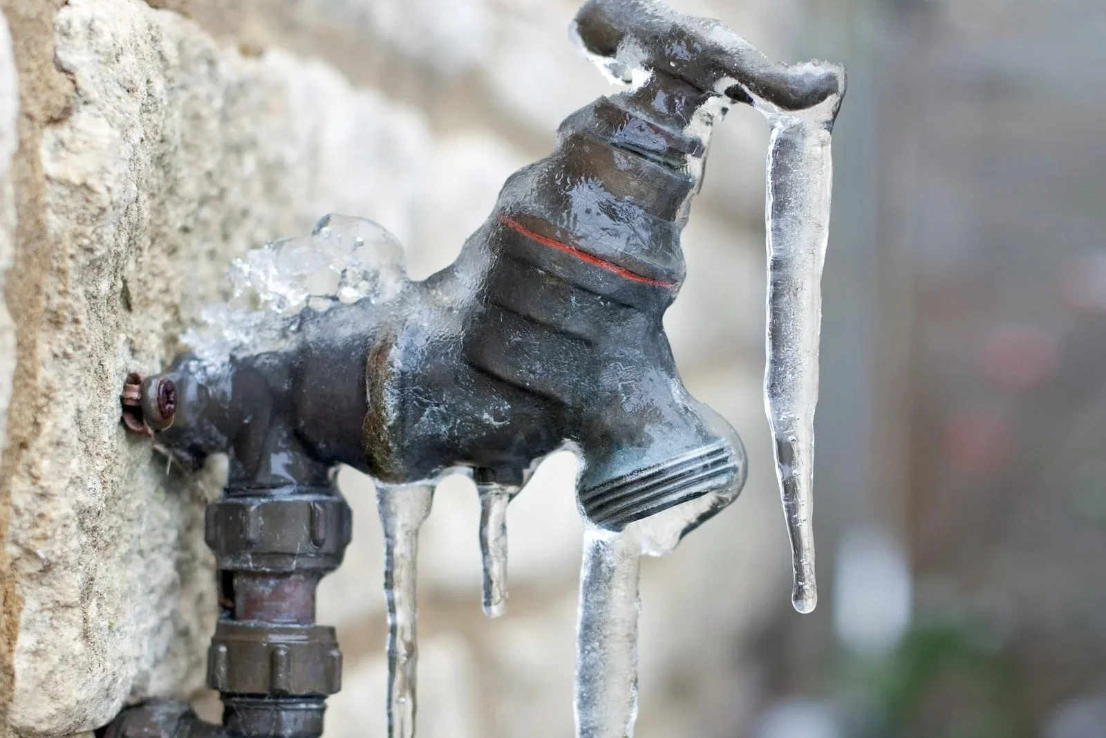 A pipe with a valve is covered in ice, with icicles hanging from it.