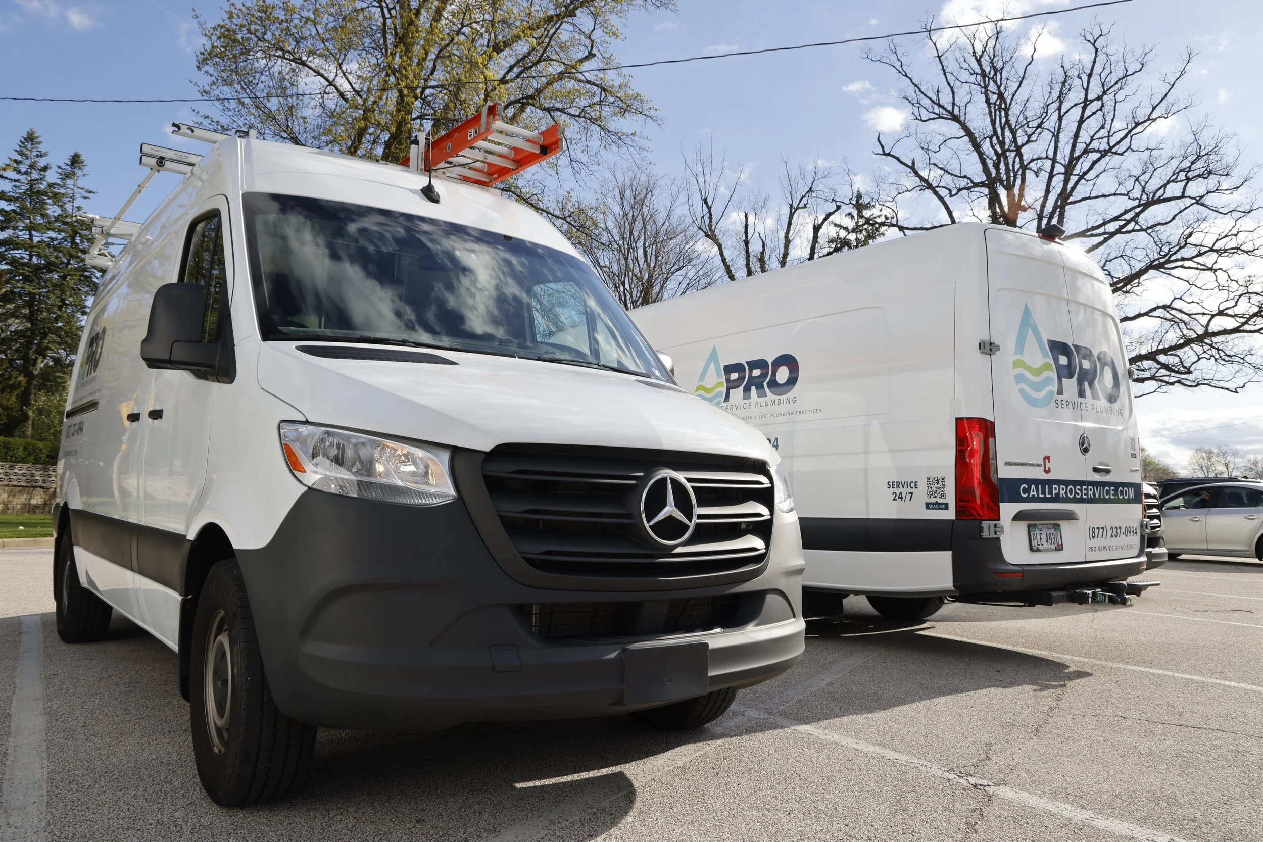 Two service vans with plumbing company logos parked in a lot on a sunny day.