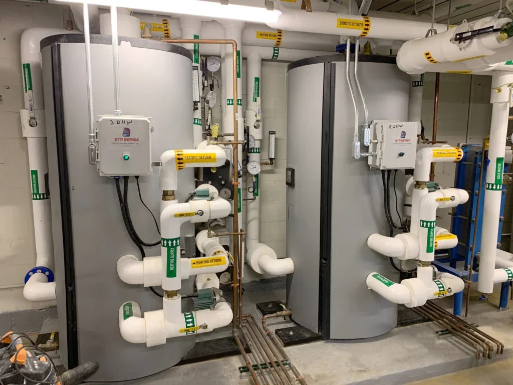 Two large industrial water heaters with pipes, gauges, and valves, installed in a mechanical room.