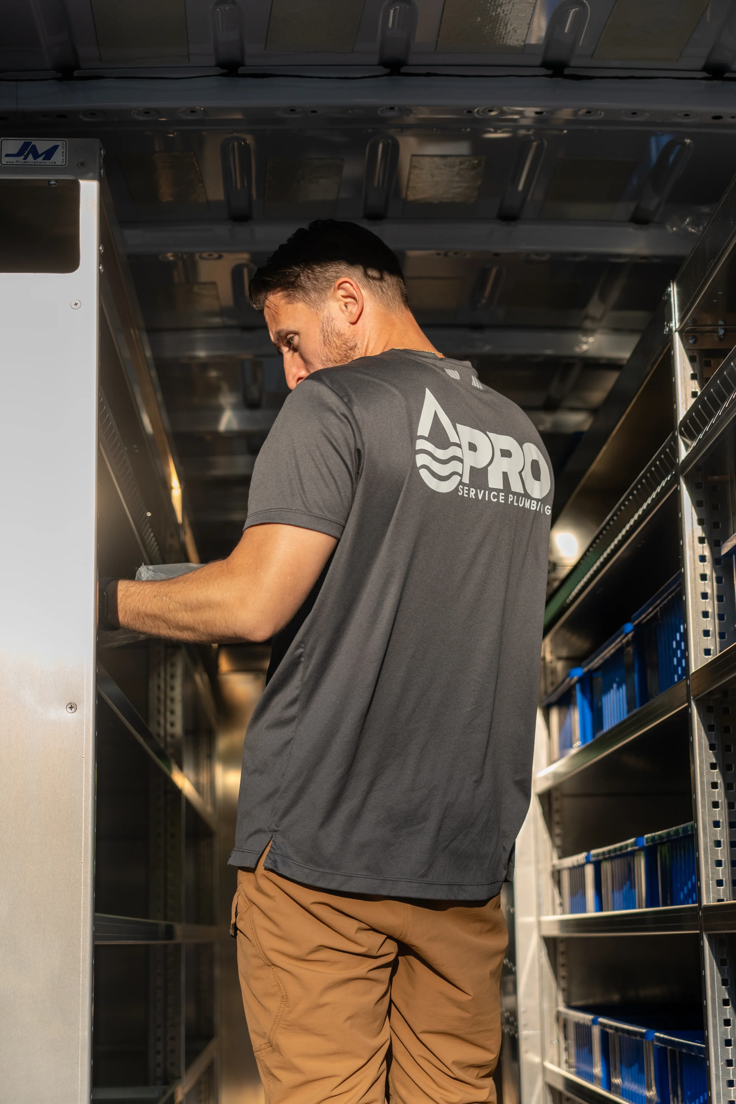 A man working in a service van, organizing tools or parts on a shelf inside the van.