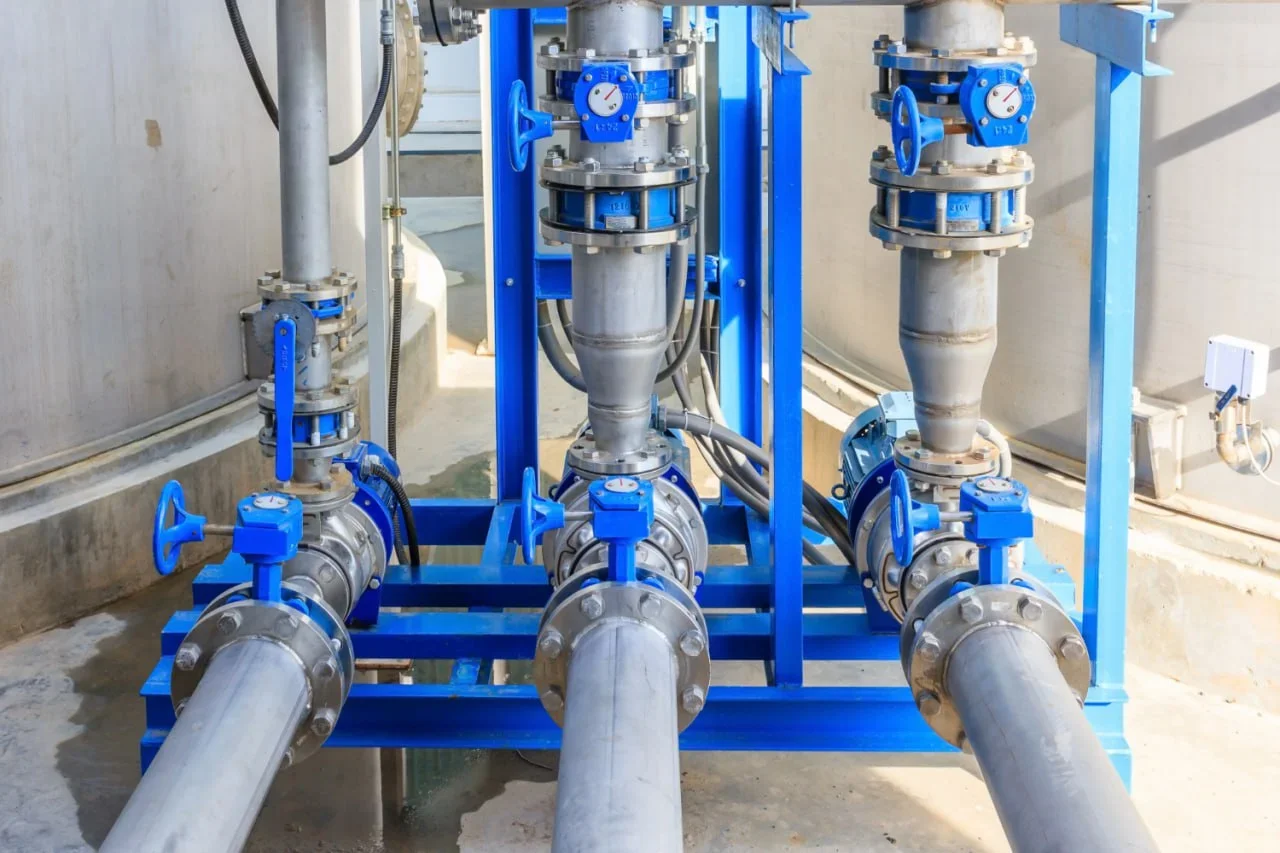 Three large industrial pipes with valves and gauges mounted on a blue metal frame in an industrial setting.