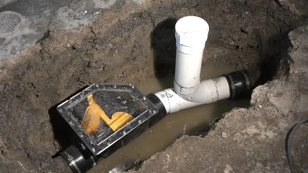 A close-up of a plumbing system with pipes in a dug trench filled with water.
