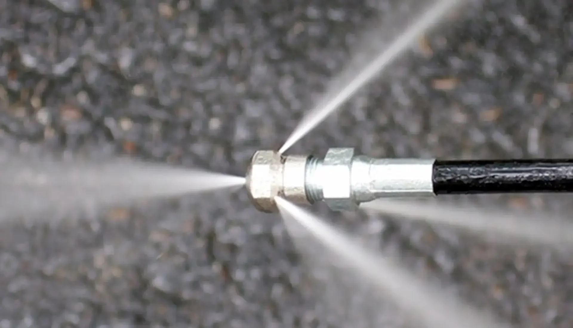 Close-up of a liquid spray nozzle spraying liquid on a gray surface.