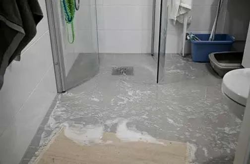 Flooded bathroom with water spilling onto the floor and a bath mat.