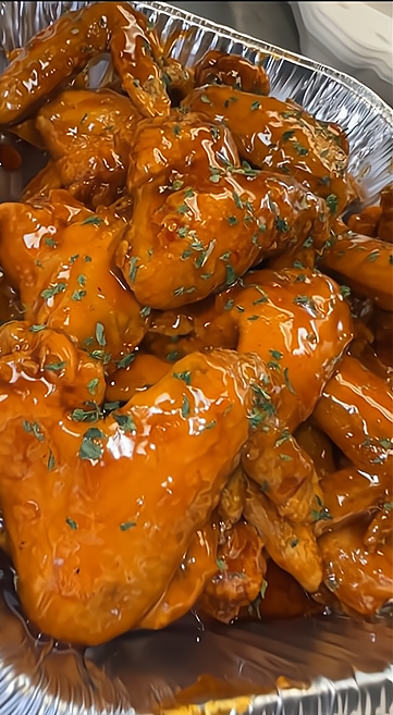 Tray of cooked chicken wings covered in orange sauce and garnished with chopped herbs.
