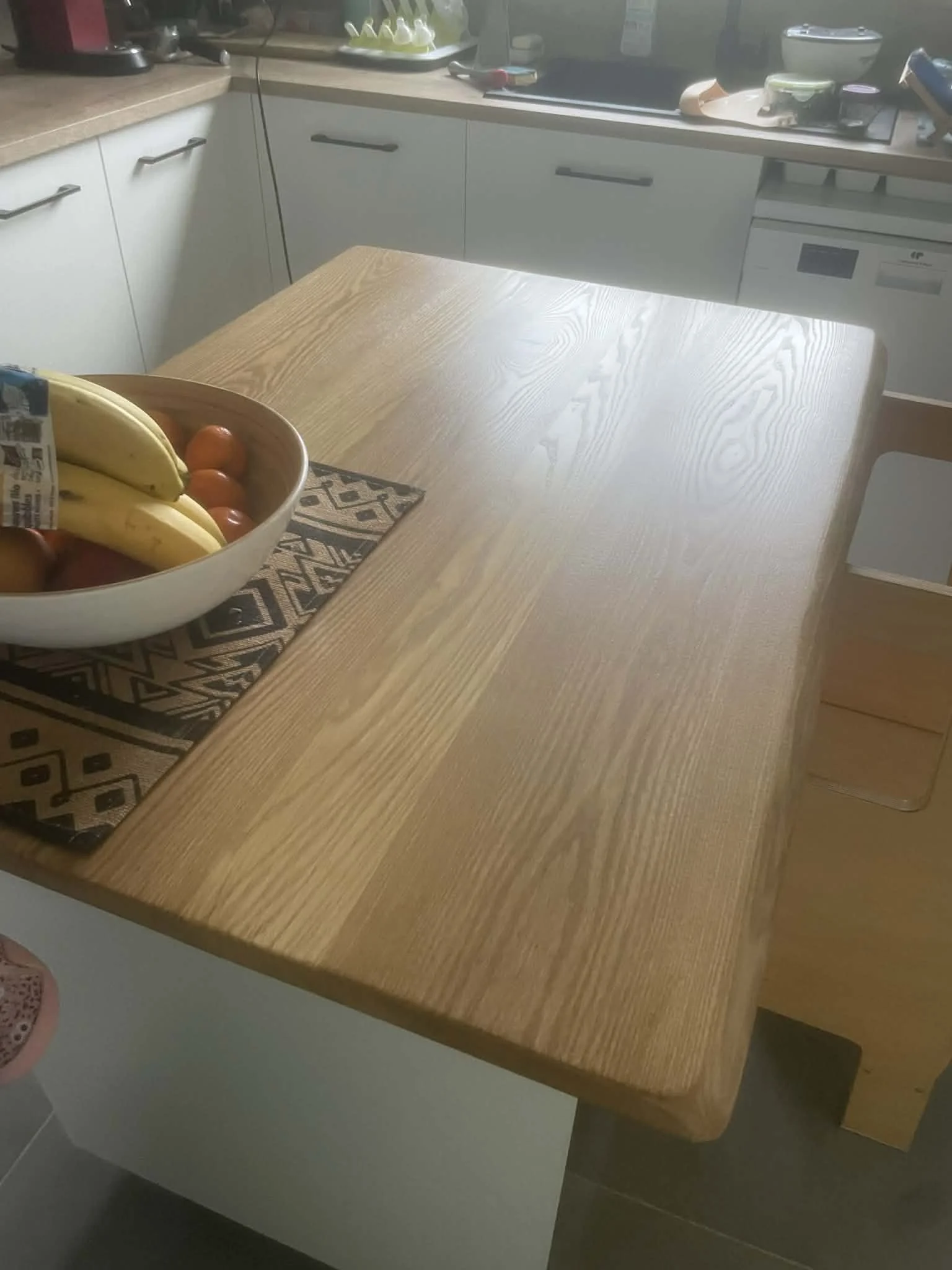 Wooden kitchen table with a bowl of bananas and tomatoes, with a patterned place mat underneath.