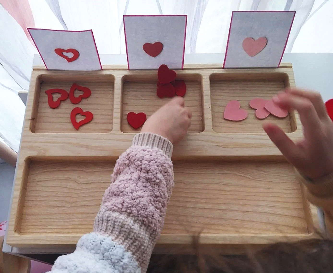 Children sorting and organizing paper heart shapes in an interactive activity with a wooden tray and cards.