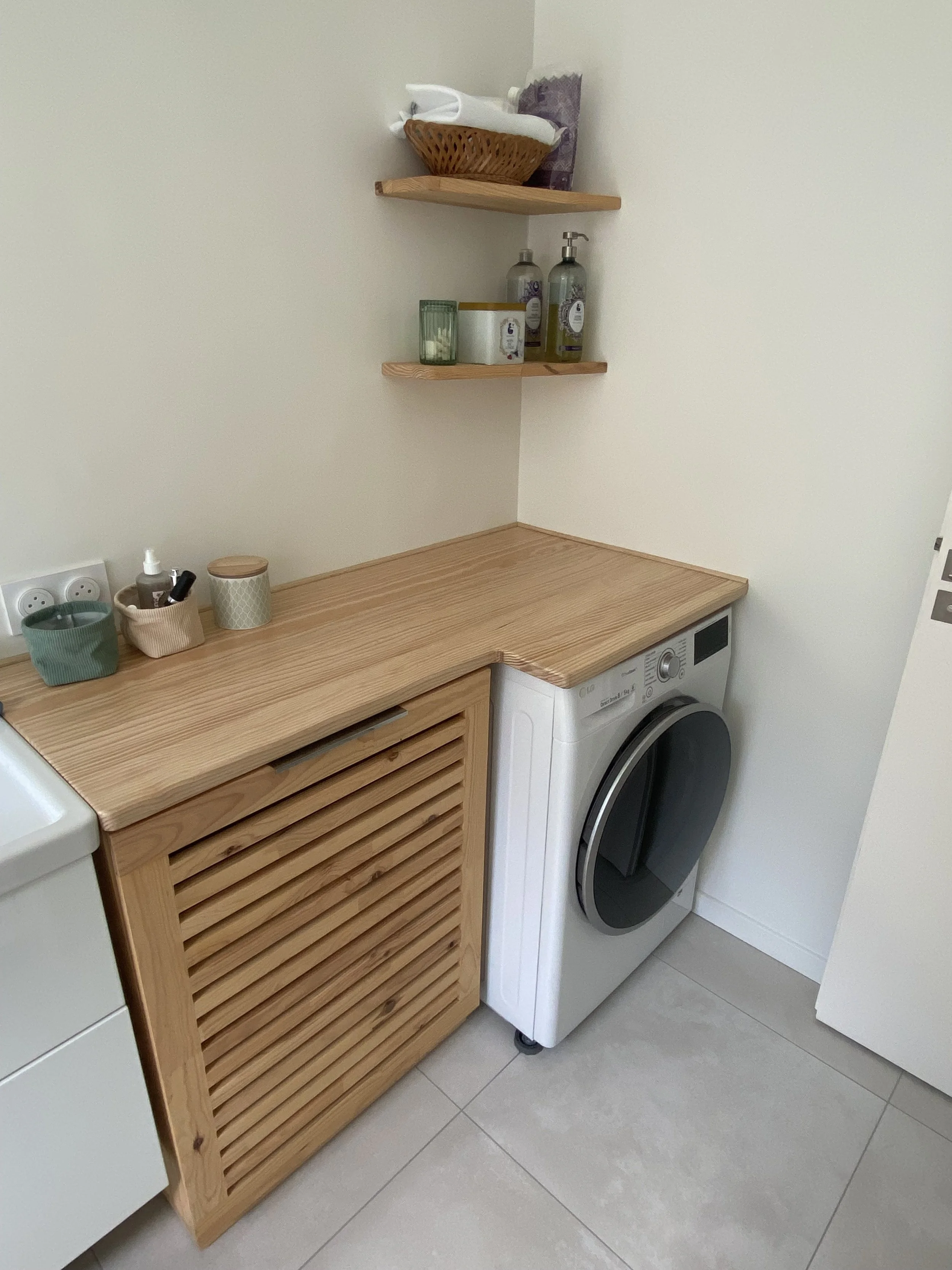 Laundry room with washing machine, wooden countertop, wall-mounted shelves with toiletries, and various containers and bottles.
