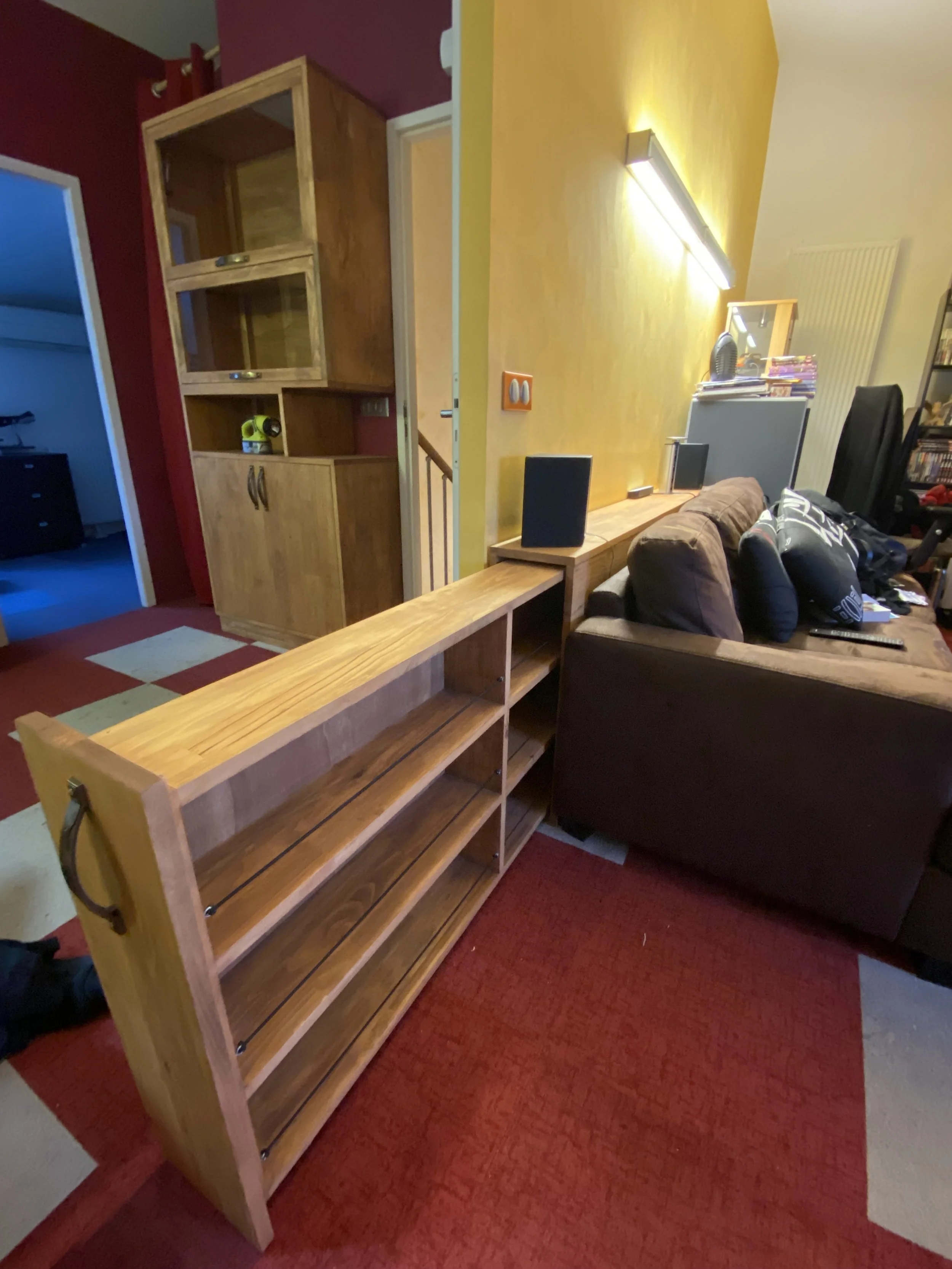 Living room with a wooden bookshelf, a brown couch, yellow and purple walls, and various electronic devices and decor items.