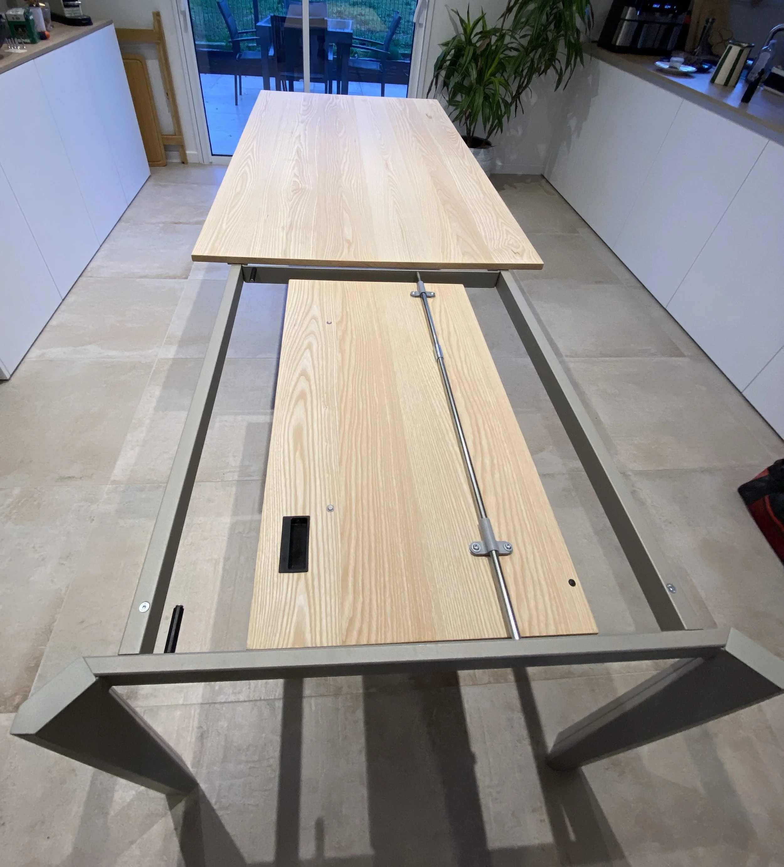 A woodworking or drafting table with a wooden surface, metal frame, and adjustable mechanism in a kitchen.