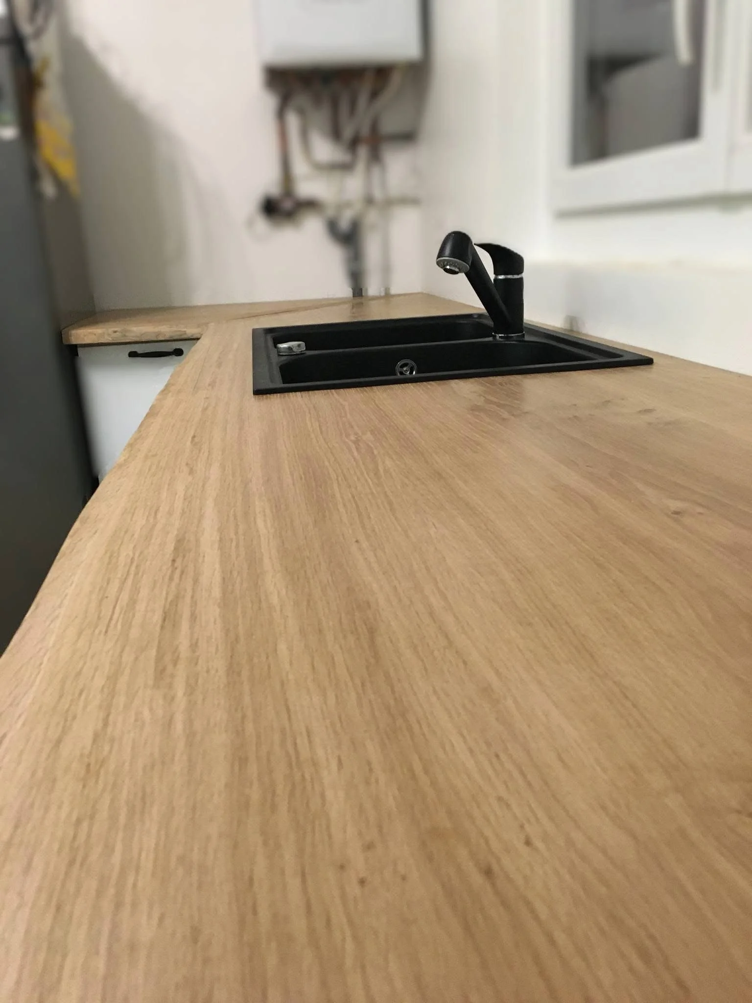 View of a black kitchen sink with a faucet, set into a light wooden countertop with a smooth finish, in a kitchen with white walls and cabinets.