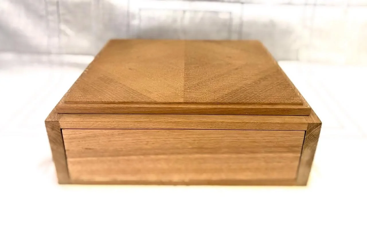 A rectangular wooden box with a smooth top, placed on a white surface, and a blurred background.