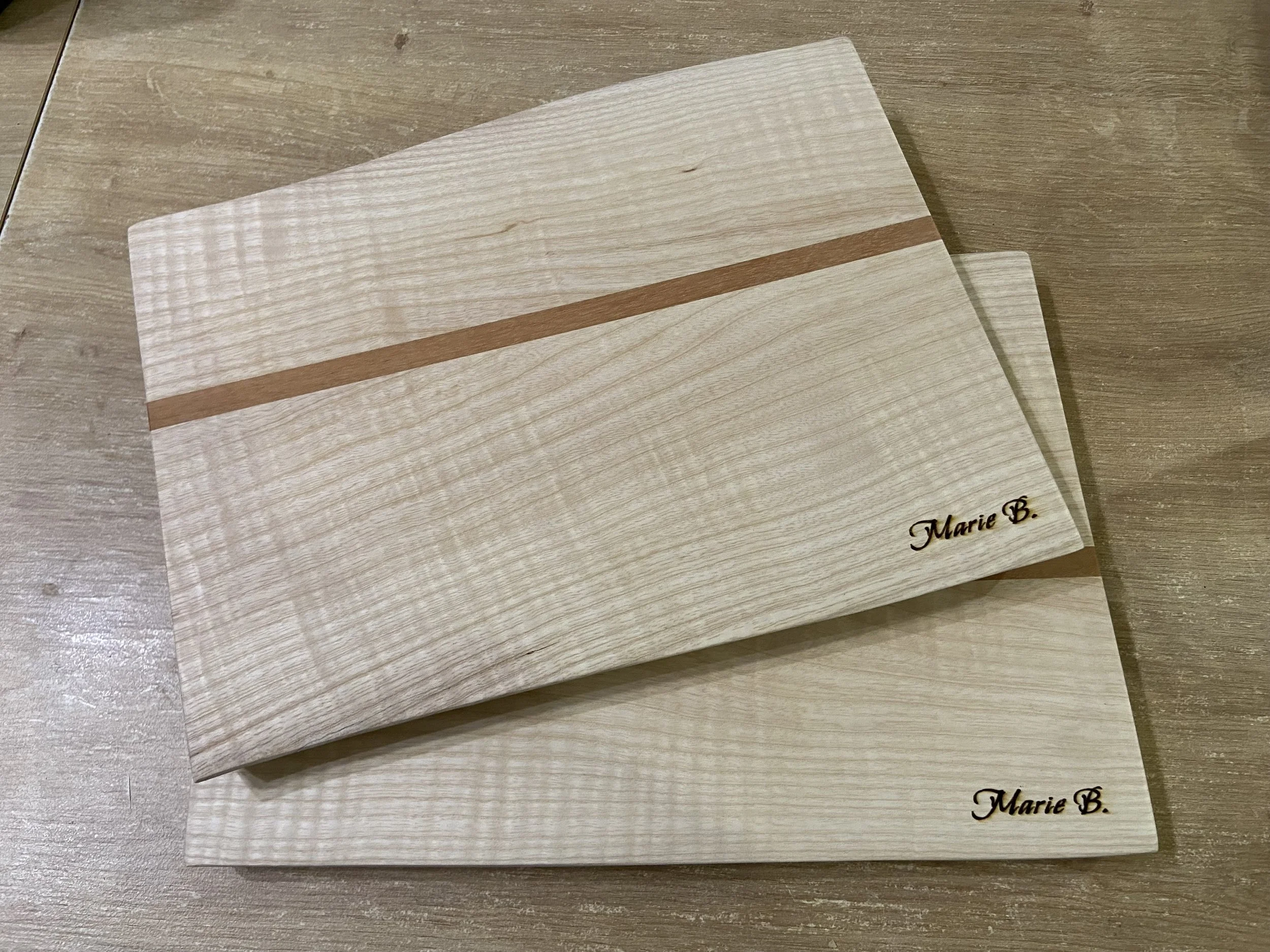 Two light-colored wood sample boards with a darker stripe and the name 'Marie B.' engraved in black.