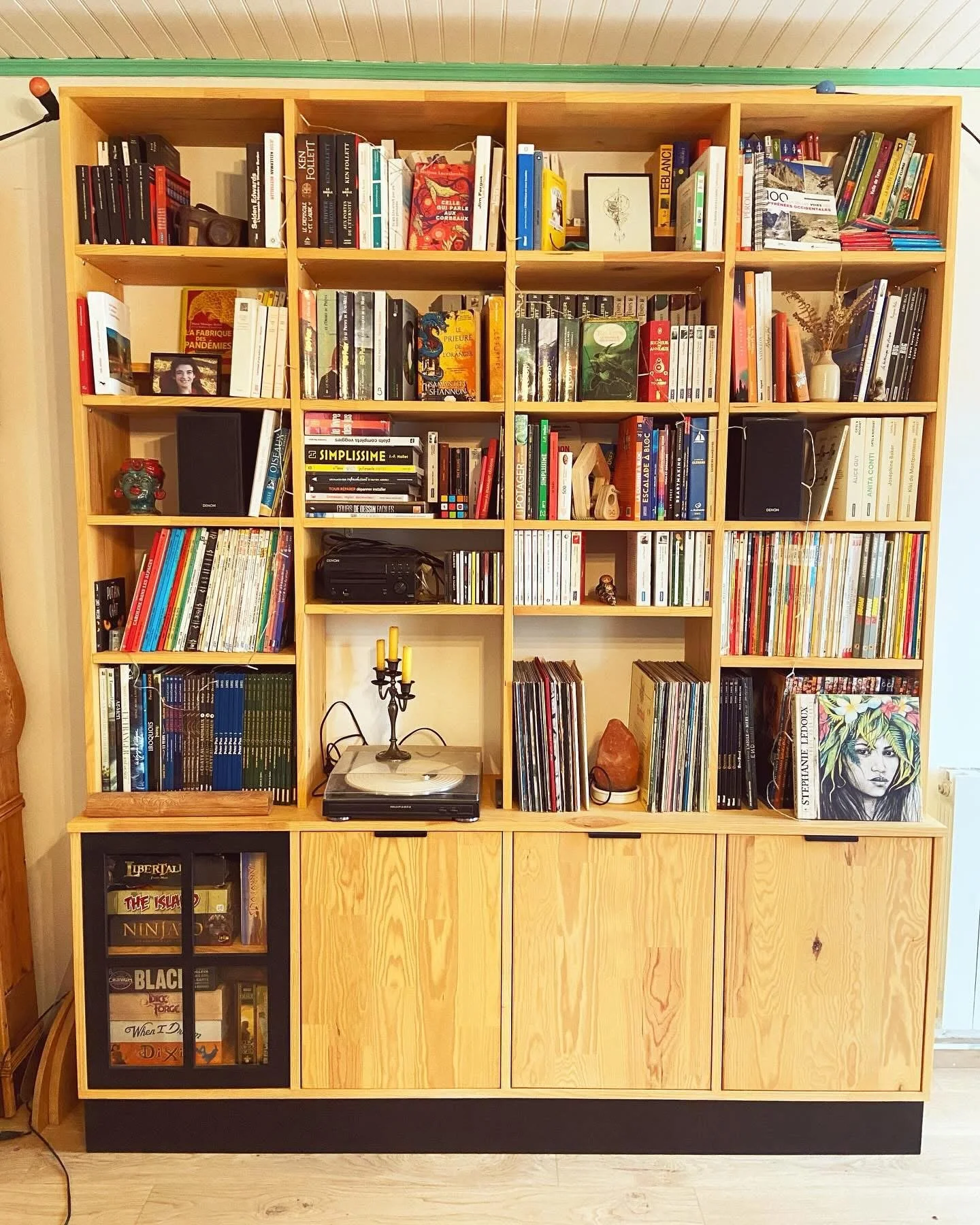 A wooden bookshelf filled with books, decorative items, a turntable, and speakers. The shelves are divided into multiple compartments with a cabinet at the bottom.