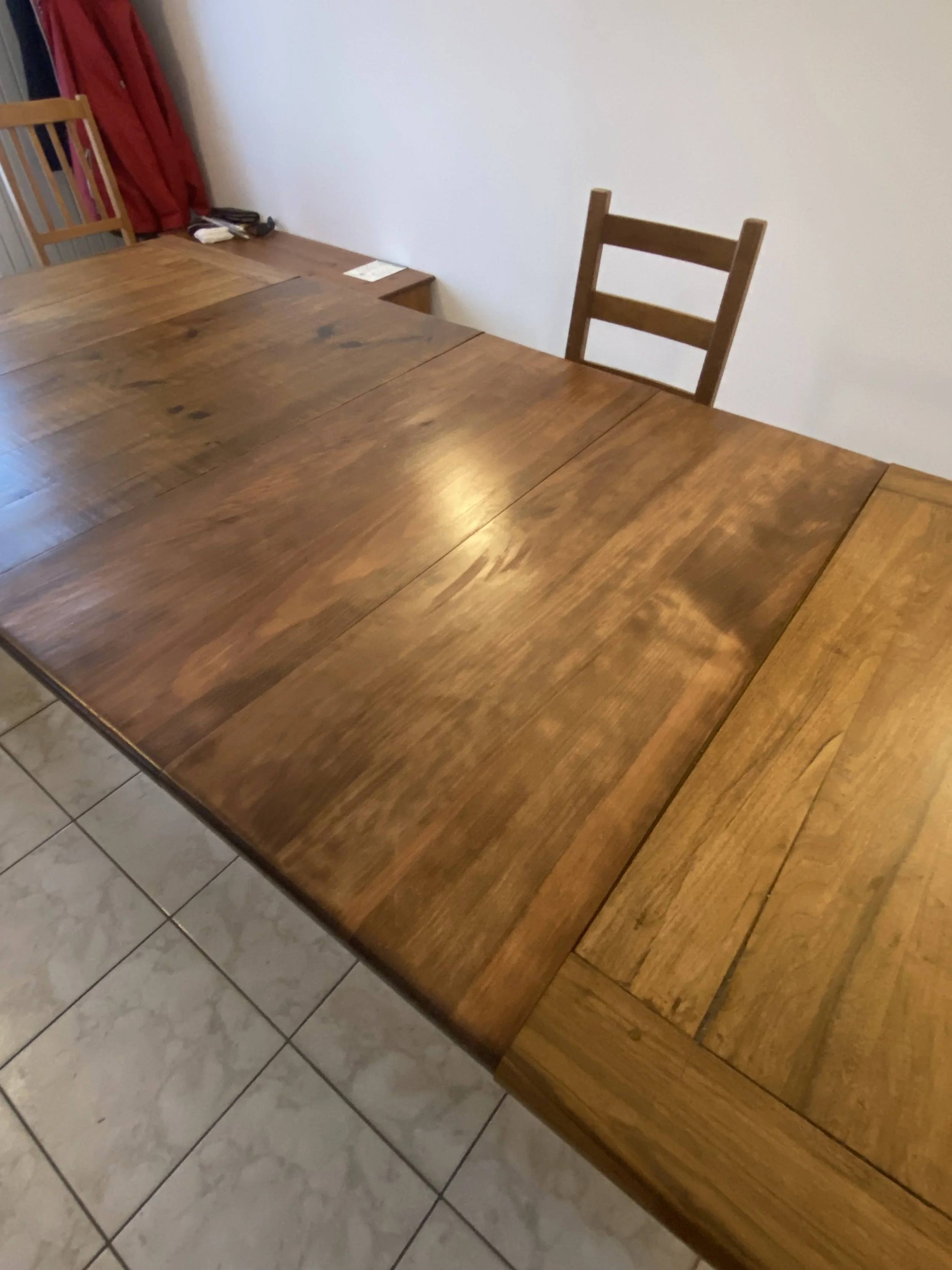 Wooden dining table with a single empty wooden chair, white wall, tiled floor, and a corner of a side table with a cordless phone and some papers.