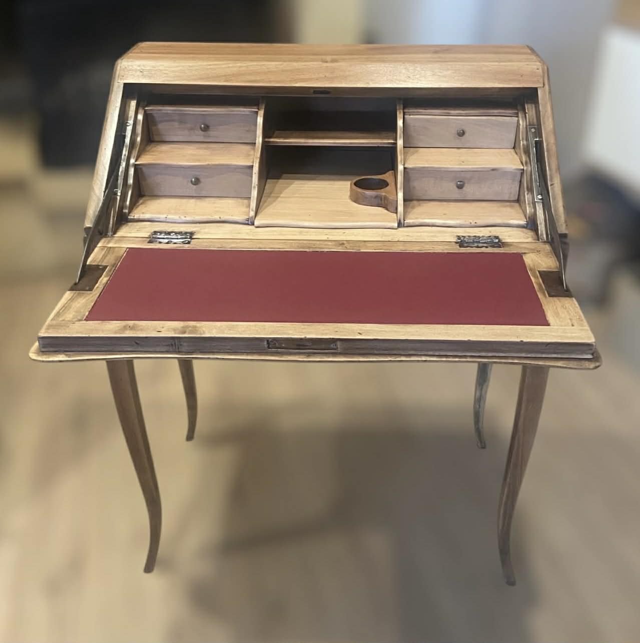 A vintage wooden secretary desk with a red writing surface, small drawers, and compartments for organizing papers and supplies.