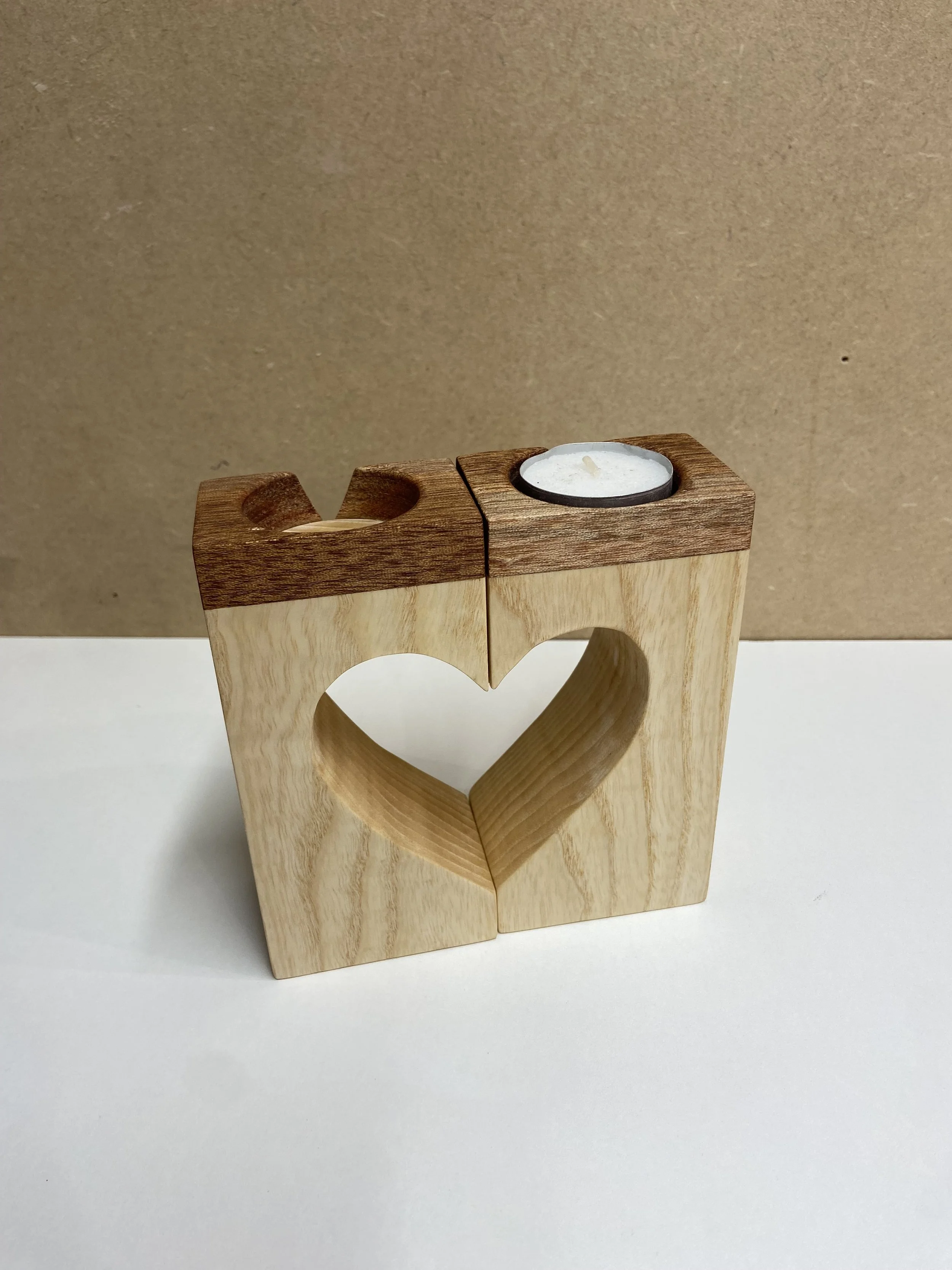 Wooden candle holder with two sections, one with a heart-shaped cutout and the other with two tea light candles, against a plain background.