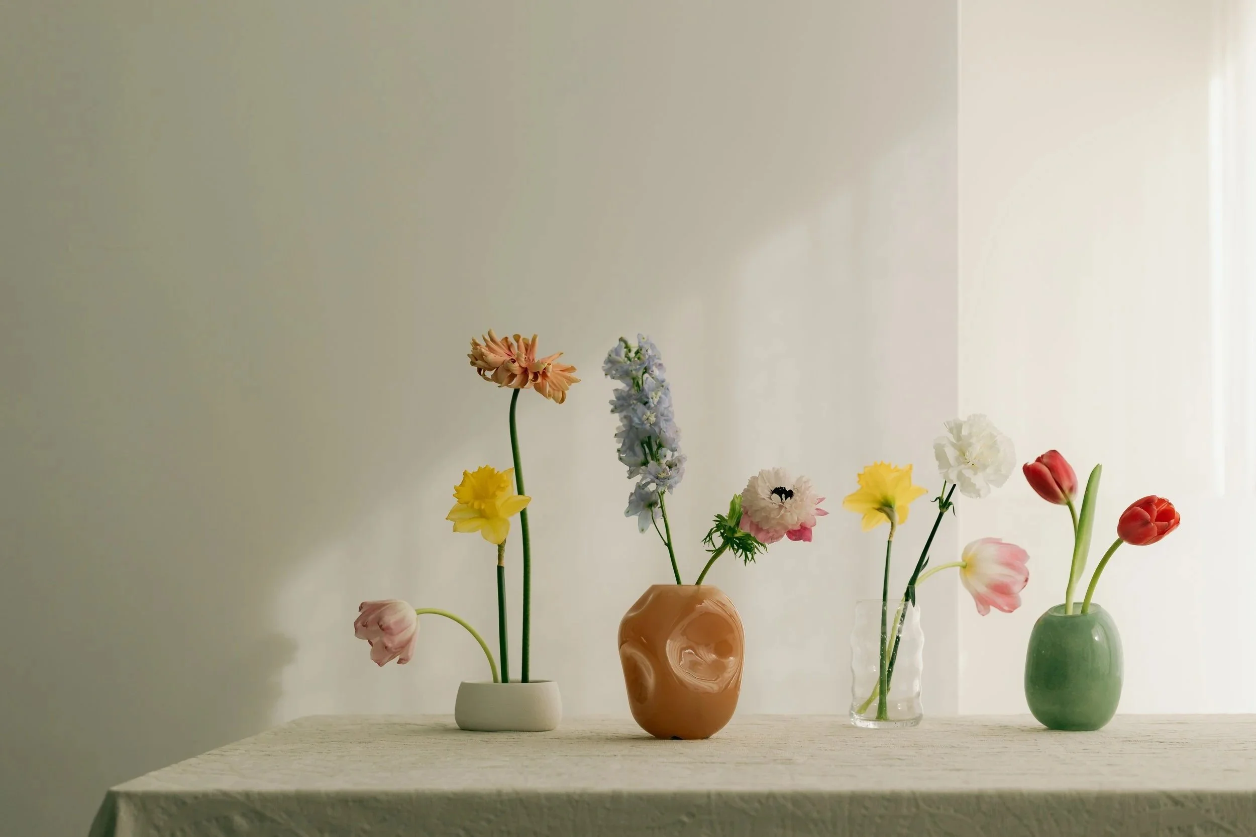 Multiple vases with colorful flowers on a table against a plain wall.