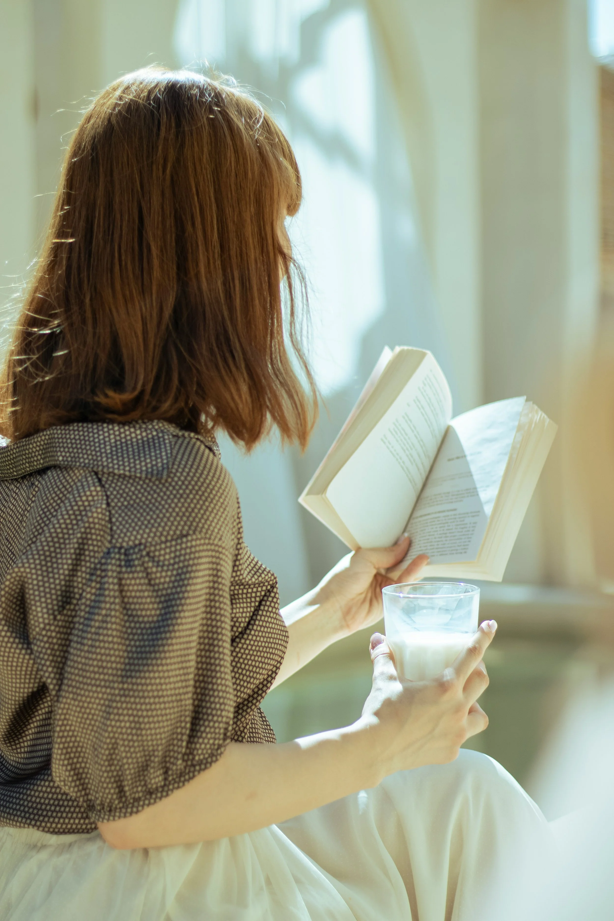 Woman with reddish hair reading a book while holding a glass of milk.