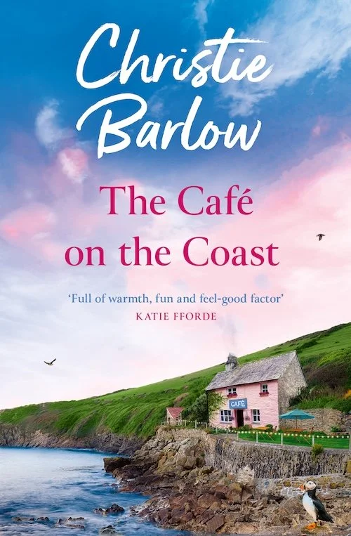 Book cover titled 'The Café on the Coast' by Christie Barlow, featuring a coastal landscape with a small pink café and a house on a grassy hill near the ocean, under a sky with clouds and birds.